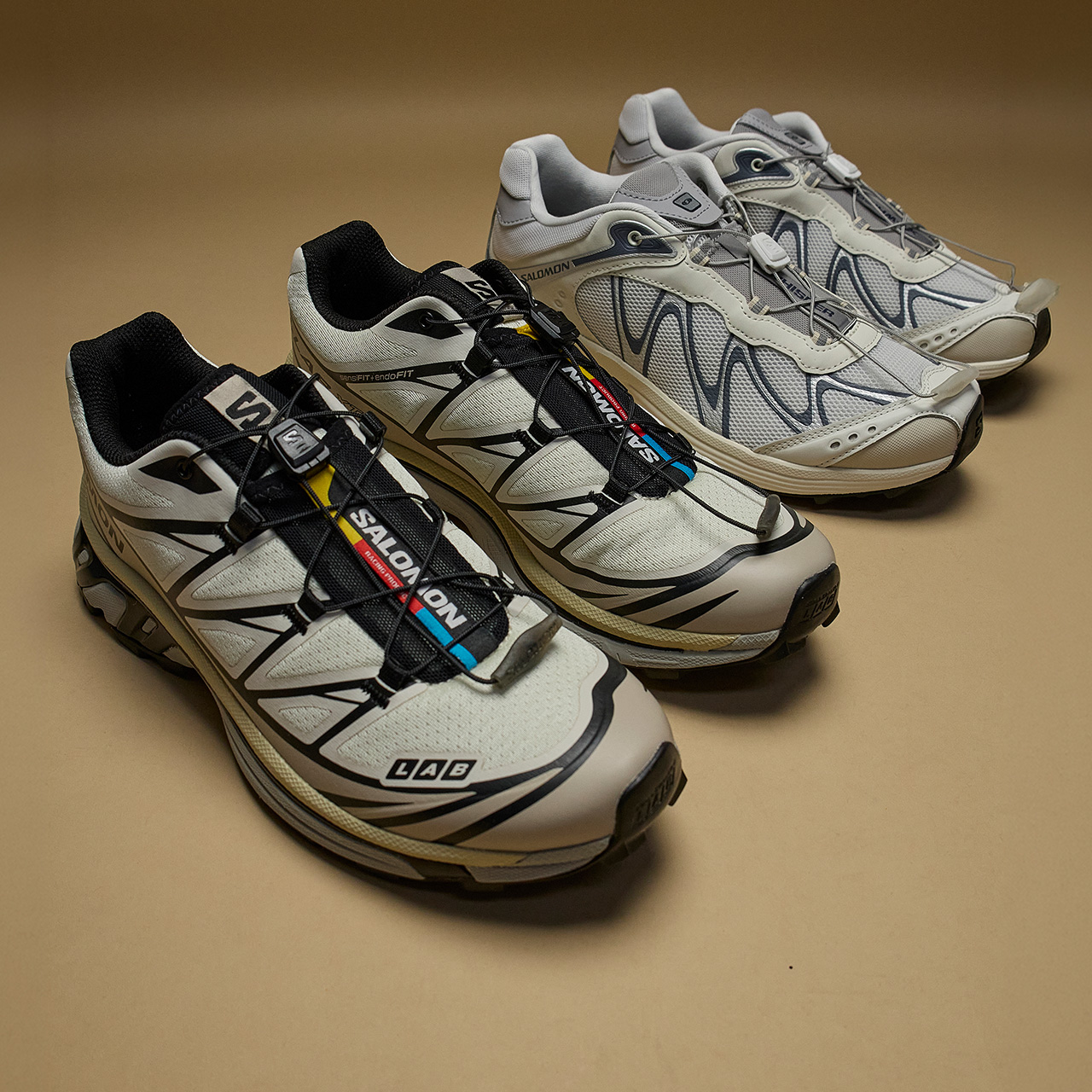 Four men's athletic trainers in cream and black colourways with contrasting stripes and branded details on neutral background