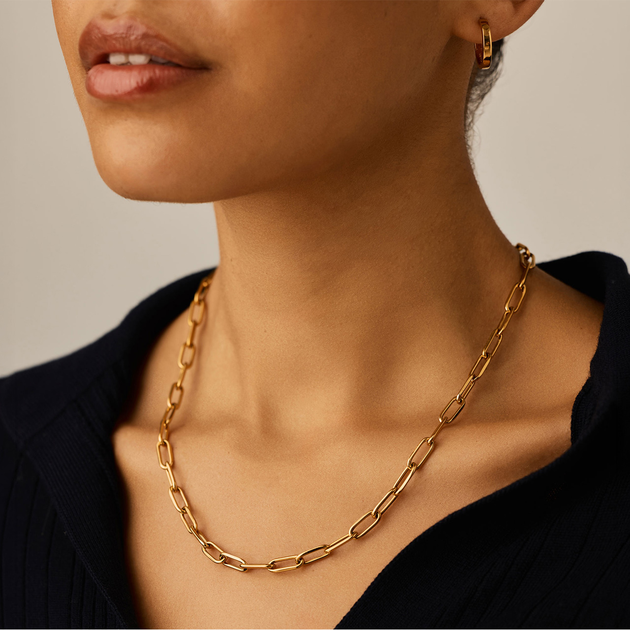 Woman wearing black top and gold chain link necklace with matching gold hoop earrings