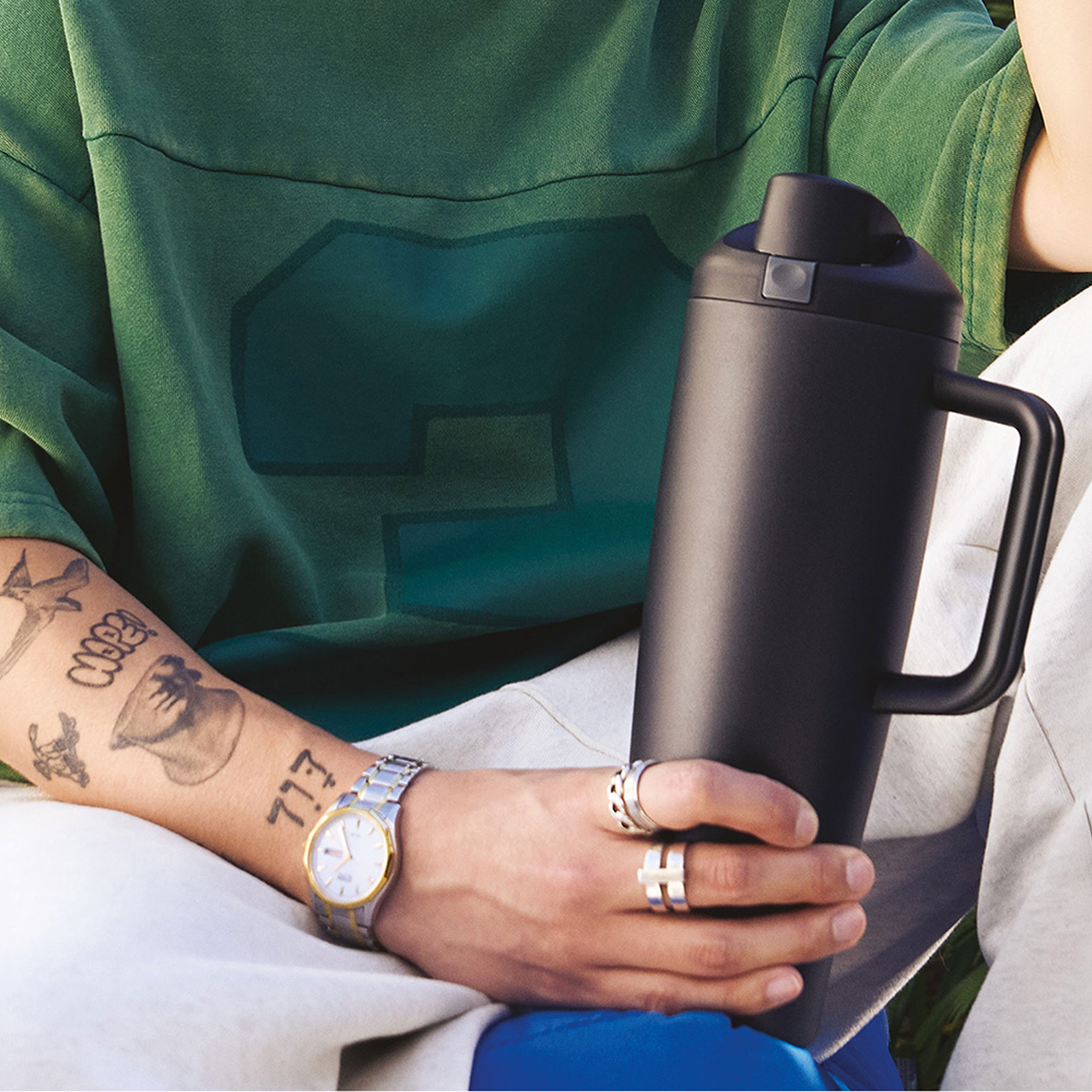 Person holding black Owala insulated water bottle with handle, wearing green shirt and accessories