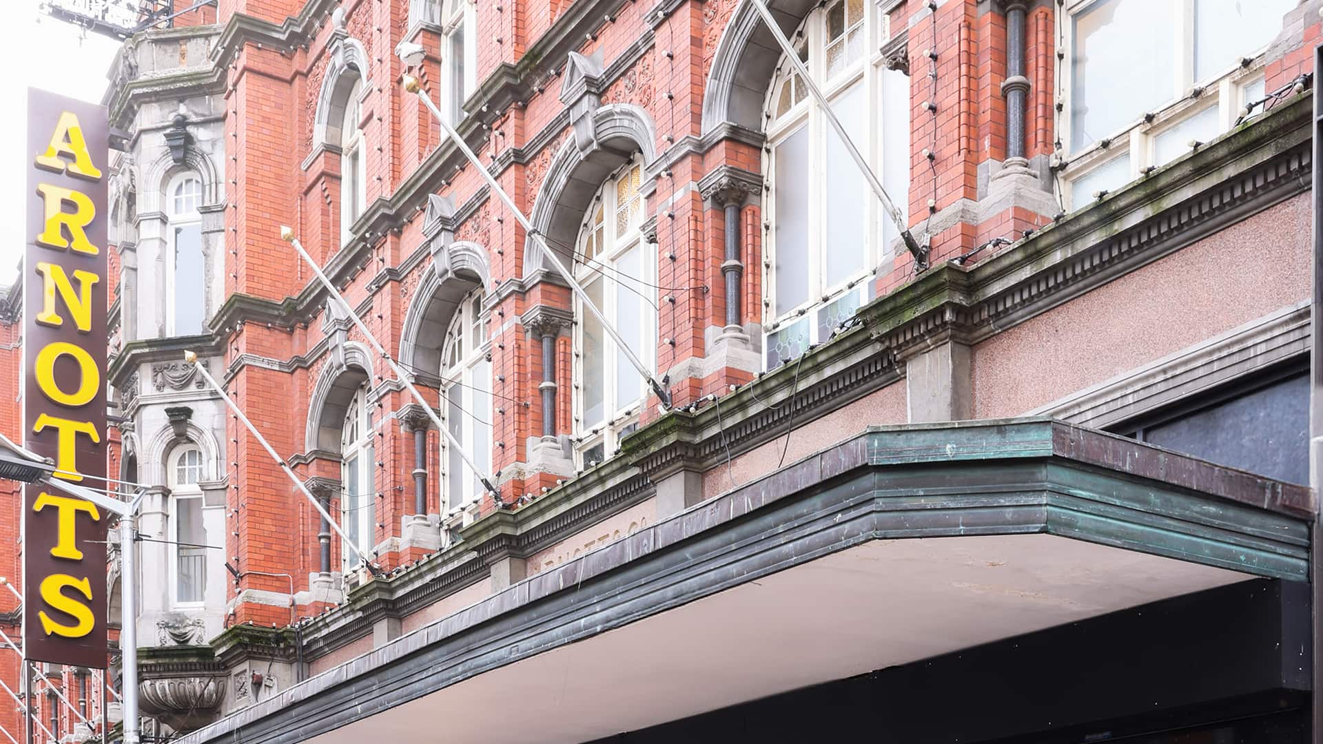 Historic red-brick building with arched windows, featuring a prominent vertical yellow sign reading 'ARNOTTS.' A green awning extends from above the entrance.