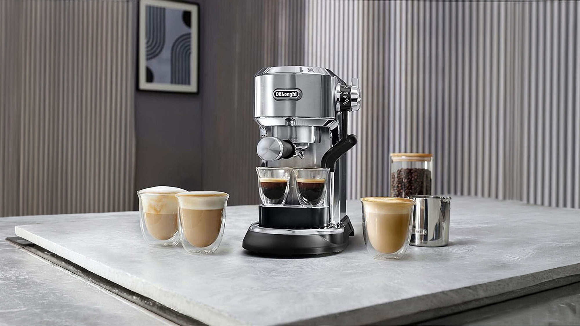 DeLonghi espresso machine with chrome finish surrounded by glasses of coffee and espresso cups on marble surface
