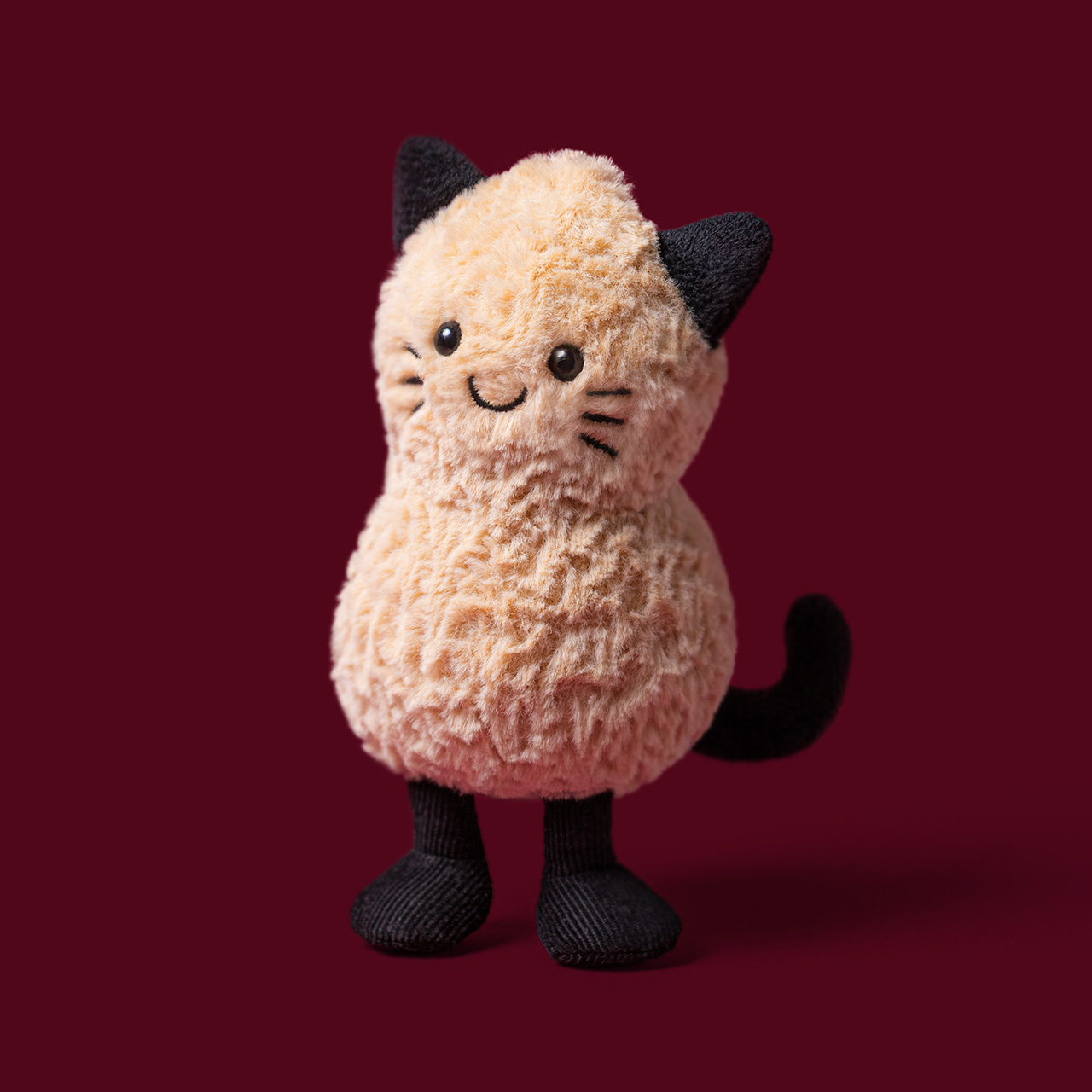 Soft plush cream and black cat toy with smiling face against deep red background