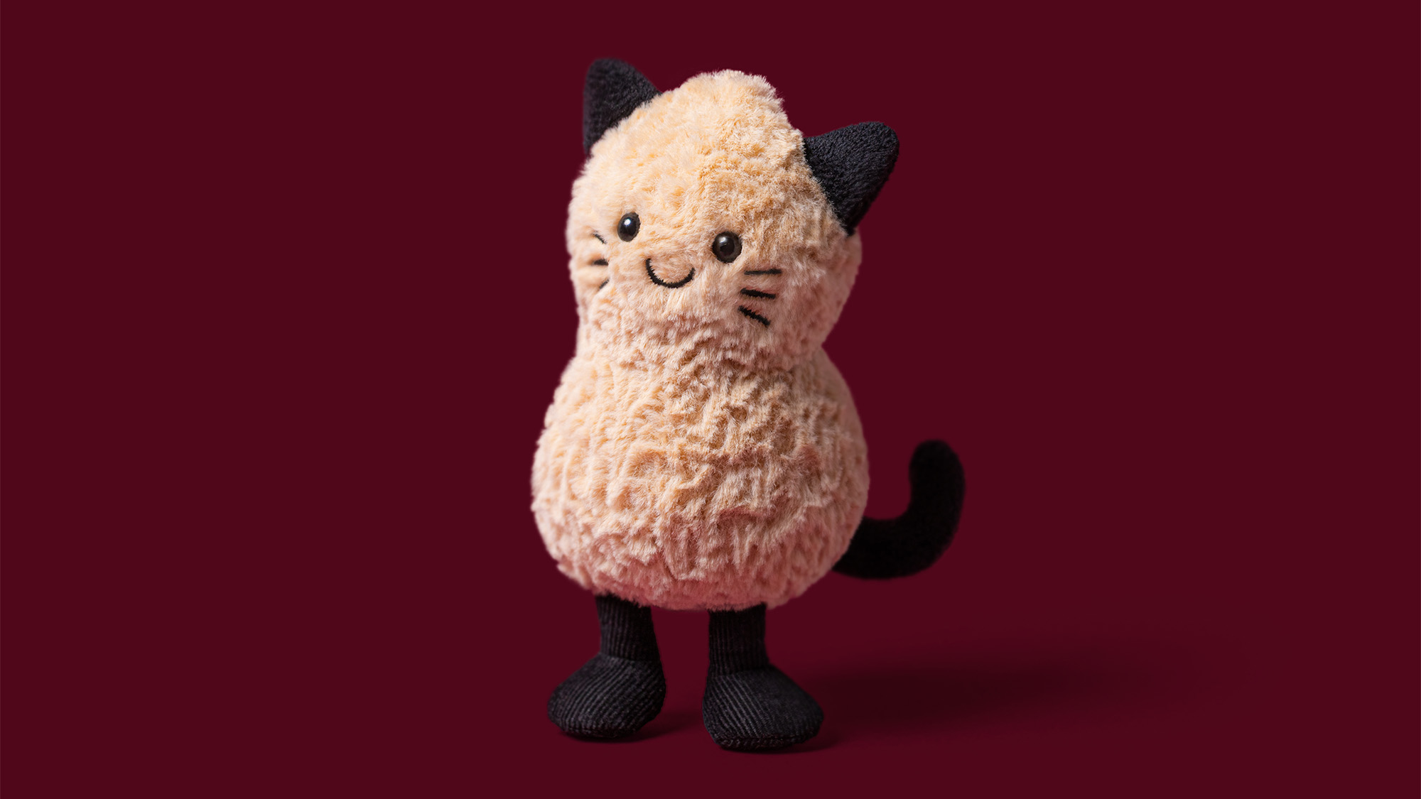 Soft plush cream and black cat toy with smiling face against deep red background