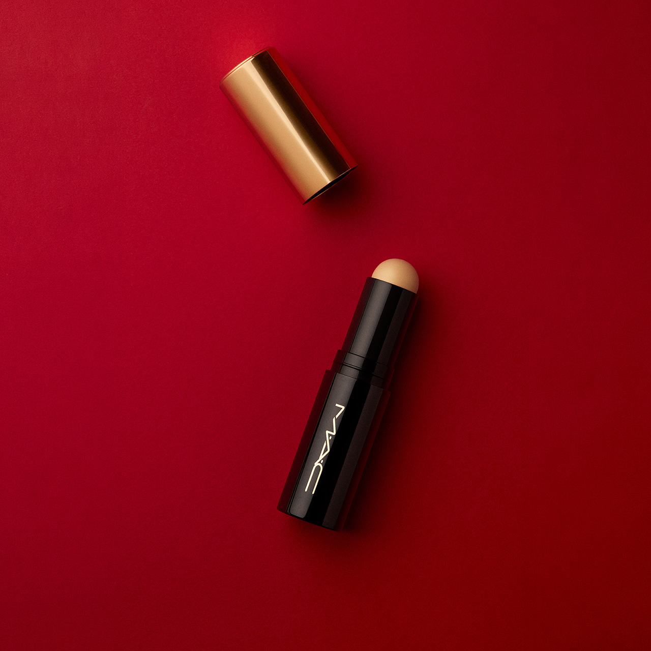 M.A.C black and gold cosmetic products including lipstick and highlighter stick on red background