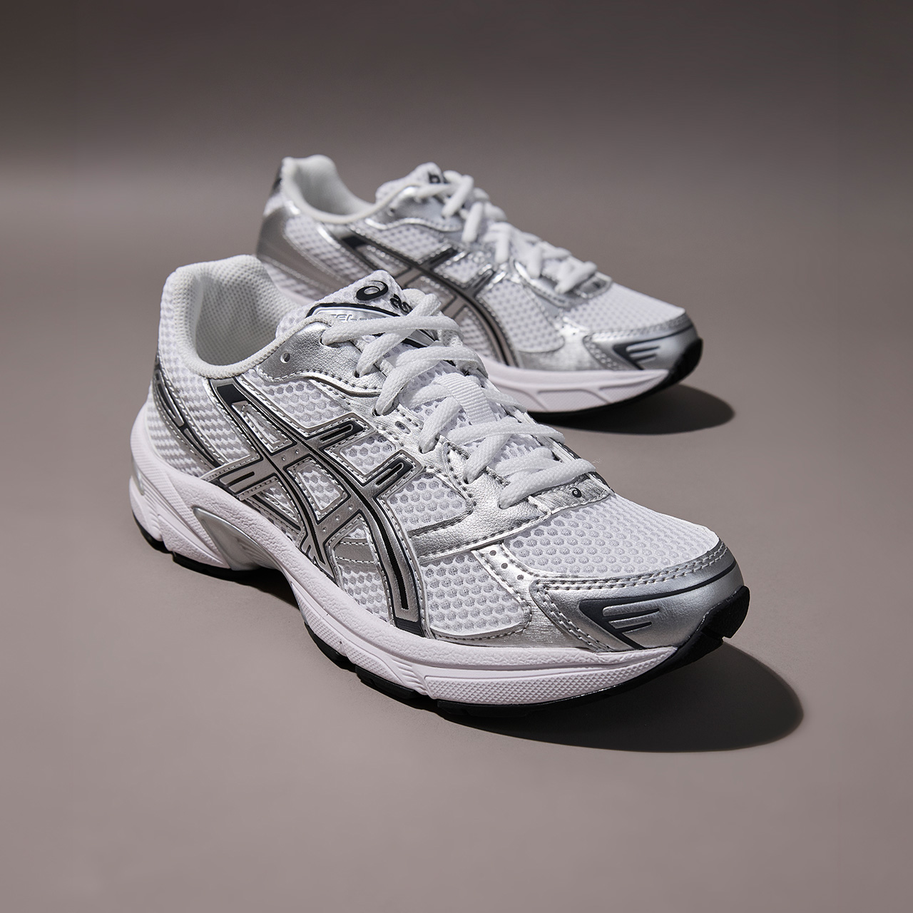 Pair of white and silver running trainers with mesh and synthetic uppers on neutral grey background