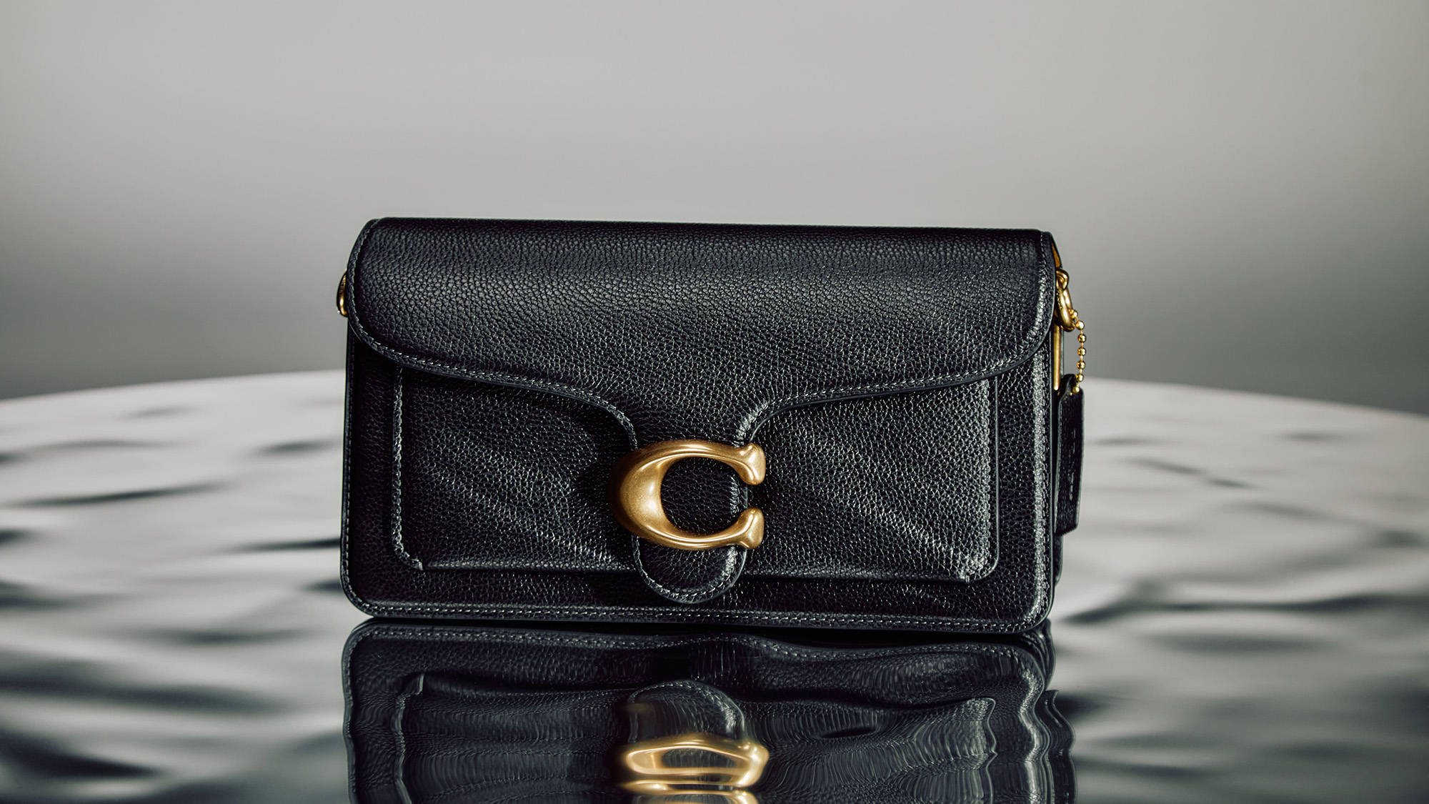 Black pebbled leather wallet with gold-toned circular hardware closure and shoulder strap detail