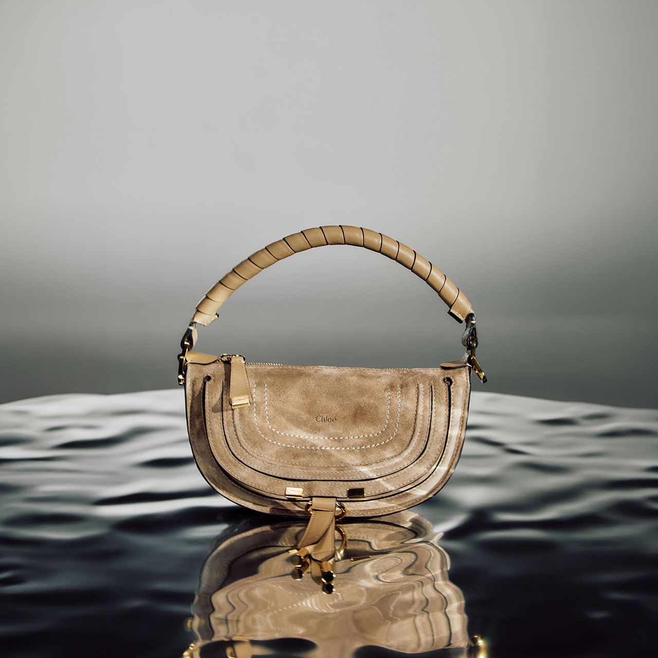 Beige suede shoulder bag with woven handle and metal hardware on water surface