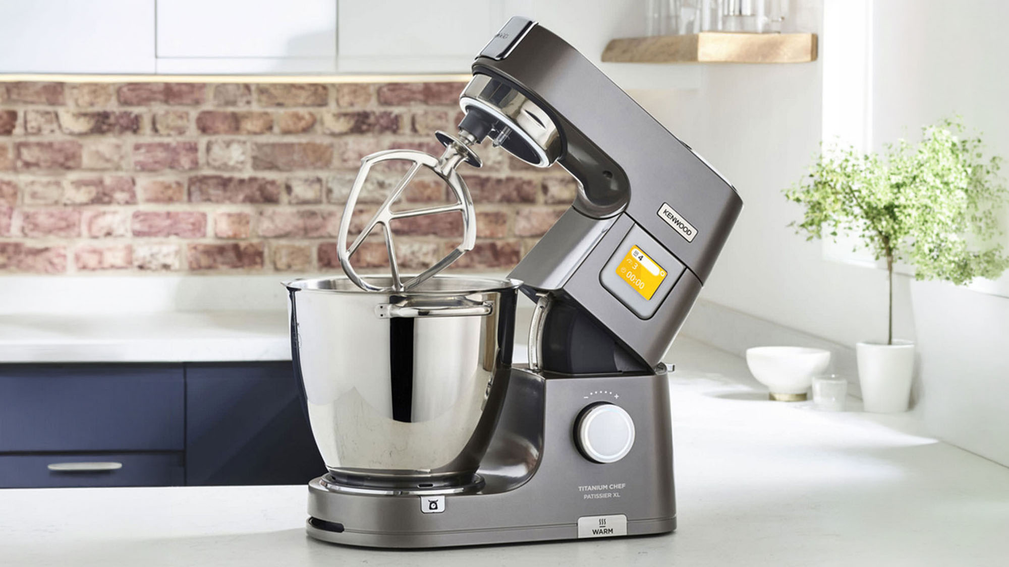 Grey stand mixer with stainless steel bowl and black handheld mixer attachment on modern kitchen worktop