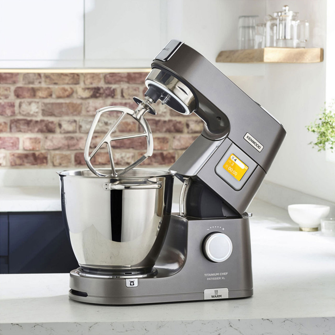 Grey stand mixer with stainless steel bowl and black handheld mixer attachment on modern kitchen worktop