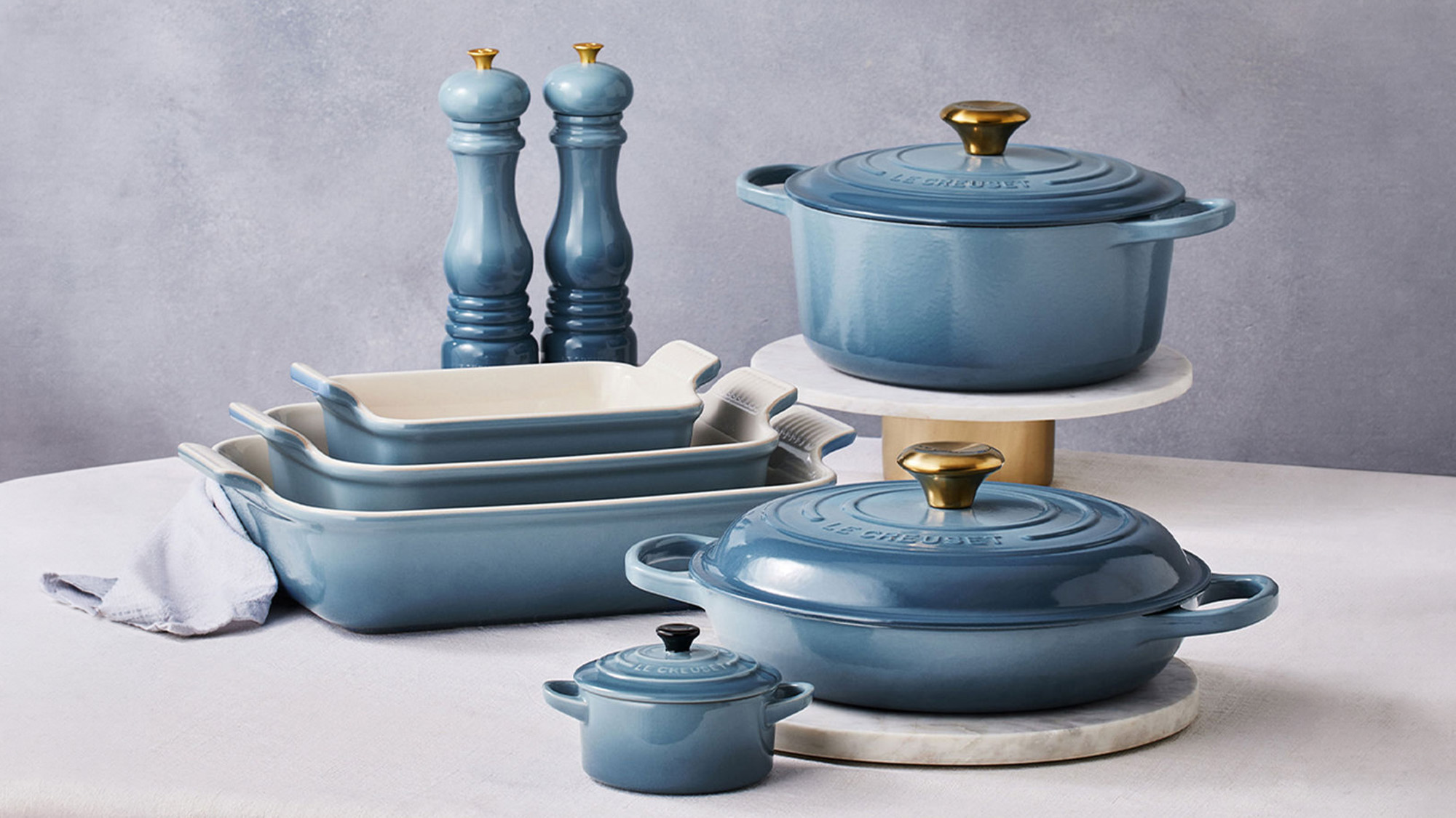 Blue cookware set including casserole dishes, rectangular baking dishes, salt and pepper mills, and cooking utensils with gold accents