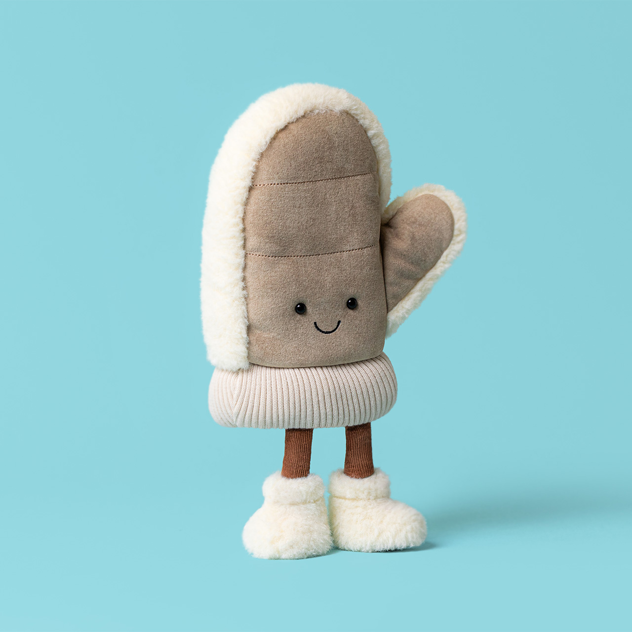 Beige and cream plush mitten toy with smiling face, white fleece trim, and brown stick legs against turquoise background