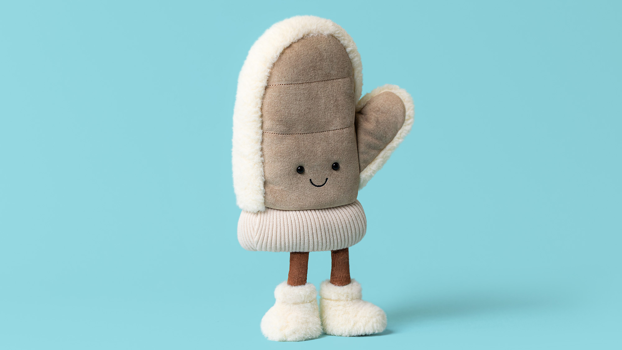 Beige and cream plush mitten toy with smiling face, white fleece trim, and brown stick legs against turquoise background