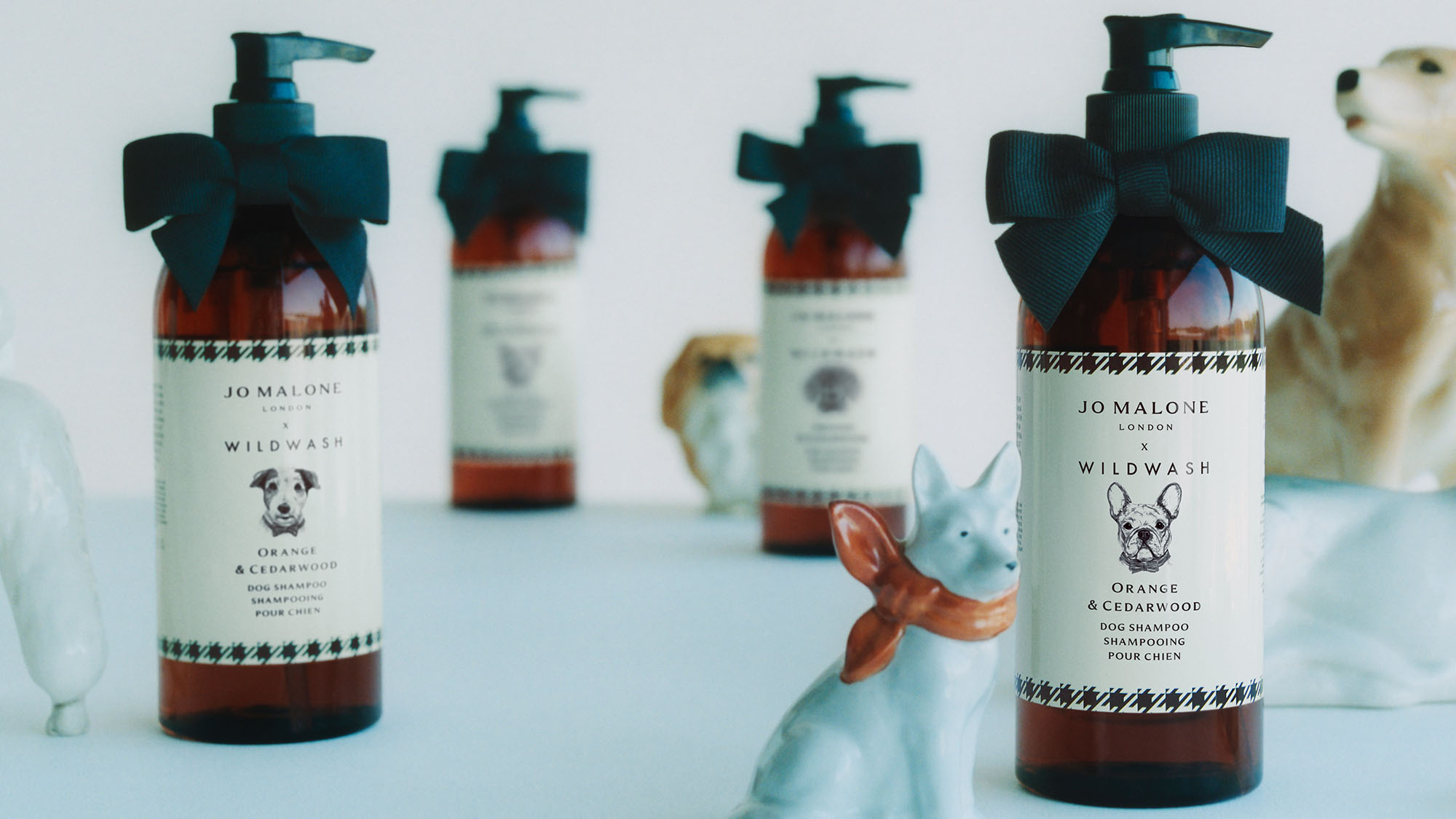 Jo Malone London x Wildwash dog shampoo bottles with turquoise bows and decorative dog figurines, orange and cedarwood scent