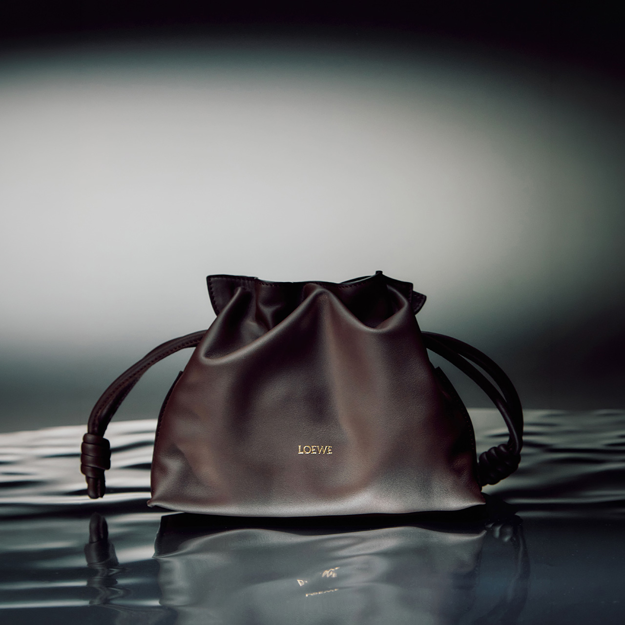 Burgundy leather drawstring bag with handles reflected in still water