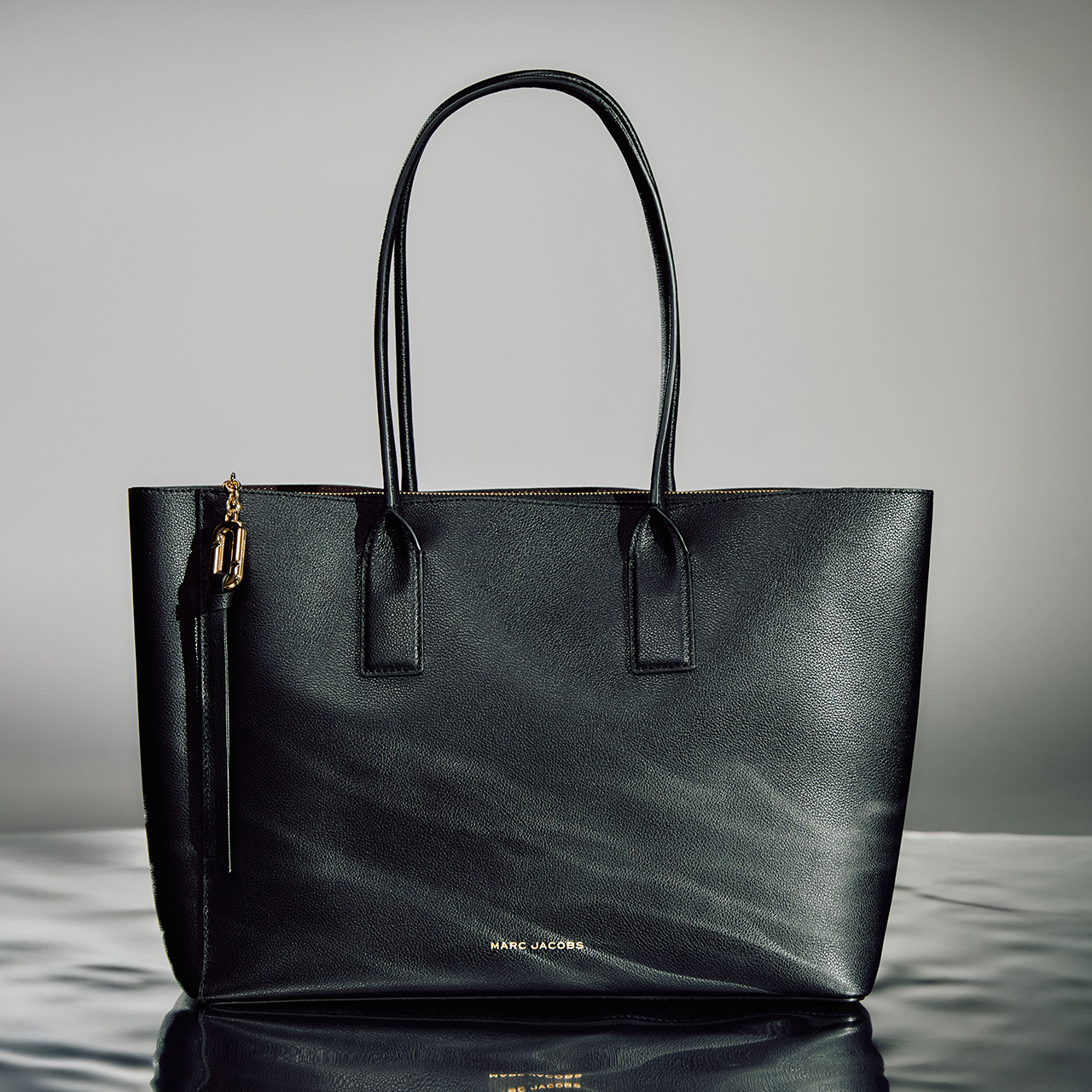 Black leather tote bag with dual handles and small gold tassel charm on side