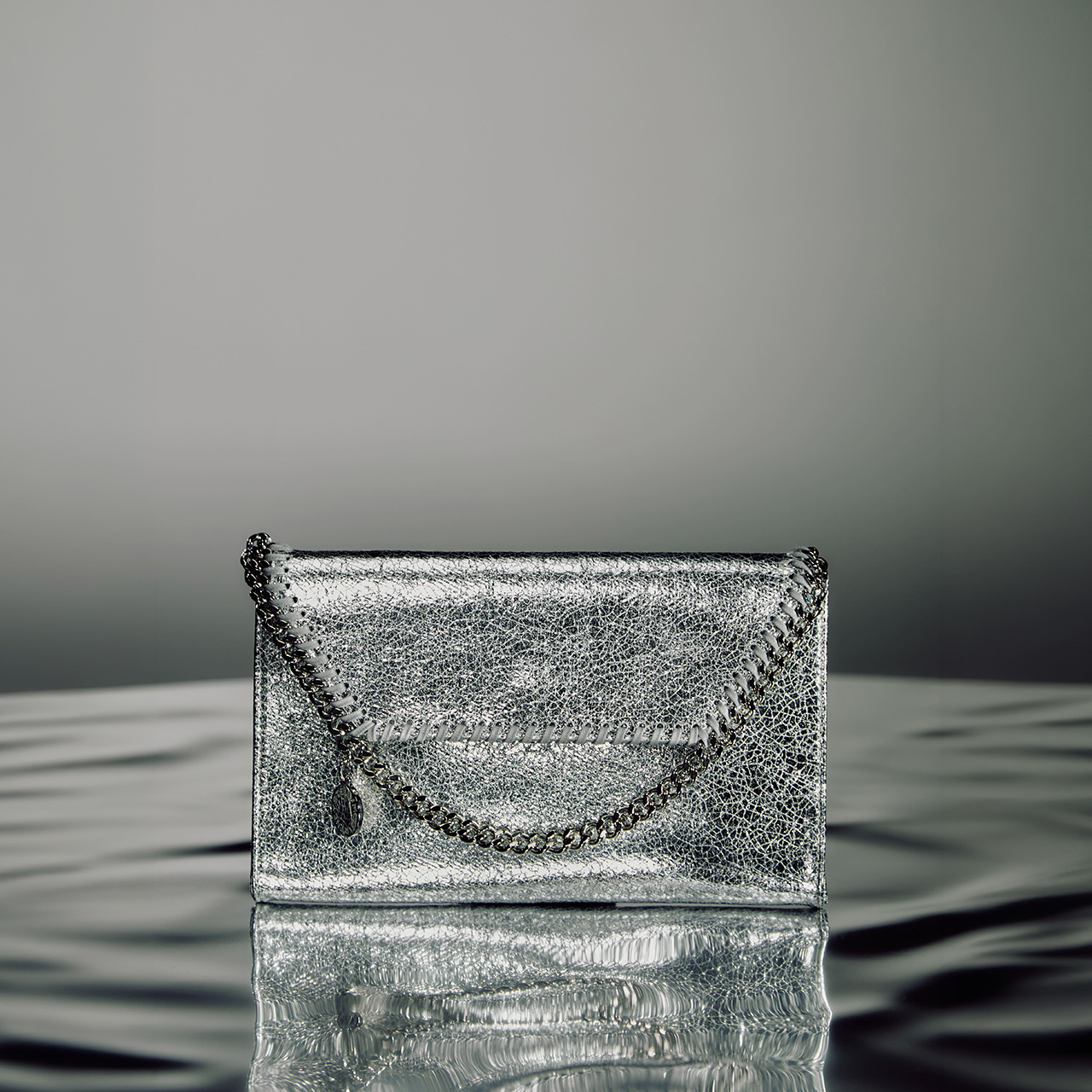 Silver metallic clutch bag with chain handle on reflective surface