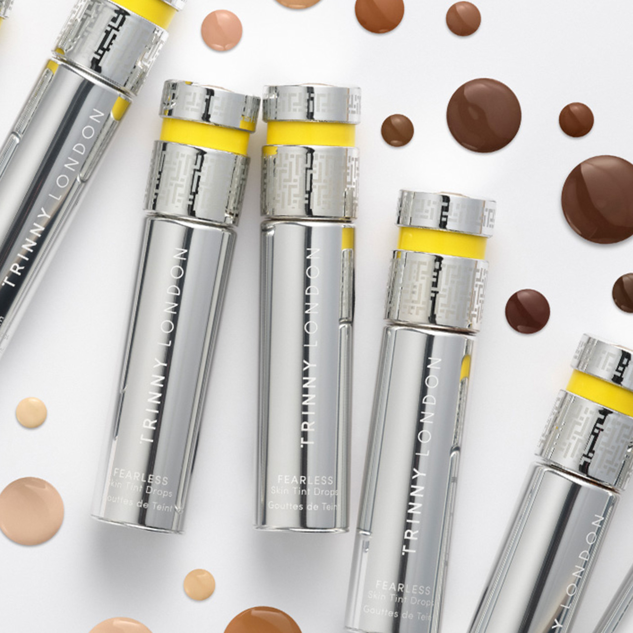 Trinny London skincare serums and drops with yellow accents surrounded by shade swatches in neutral tones