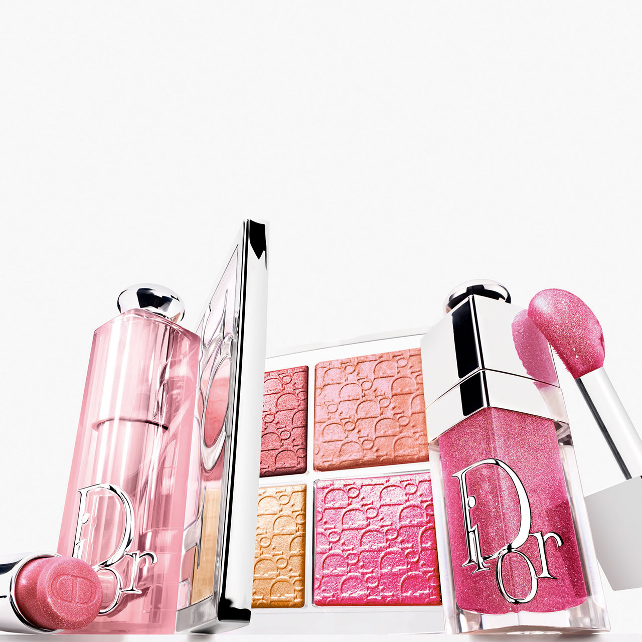 DIOR Backstage collection with pink glitter lip products, highlighter palettes in coral and pink shades, and pink liquid cosmetics