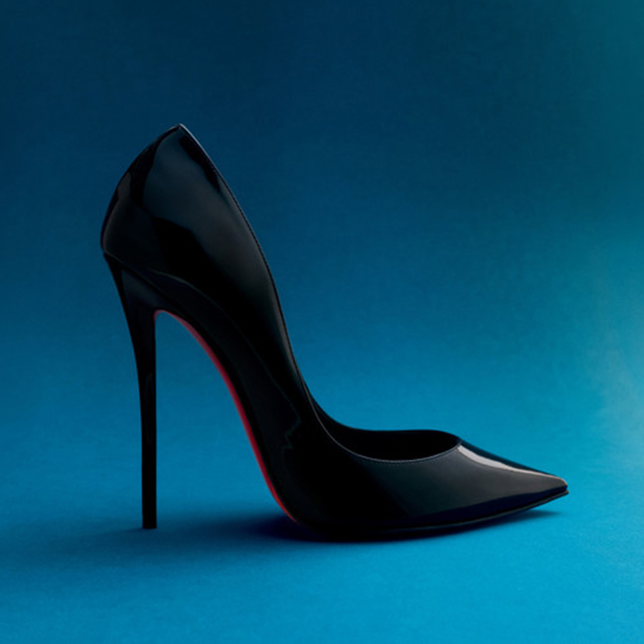 Black patent leather pointed-toe high heel pump with red sole detail, studio background