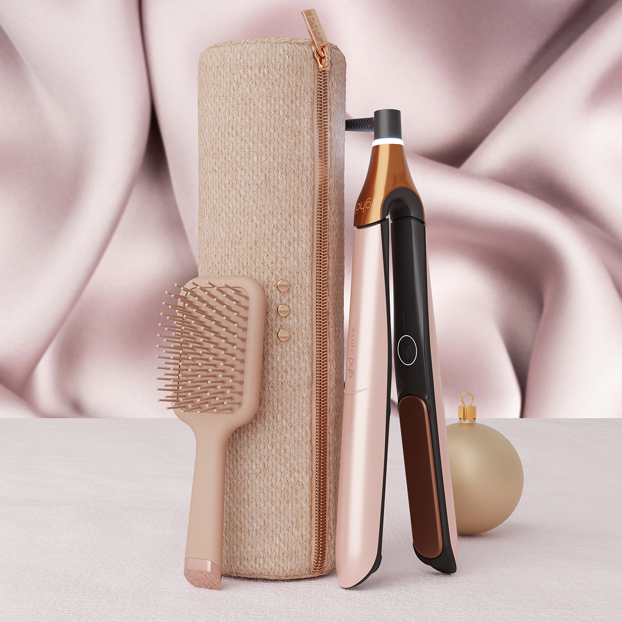 Beige fabric pouch with gold zip, paddle brush, black hair straightener, and gold ornament on pink fabric background
