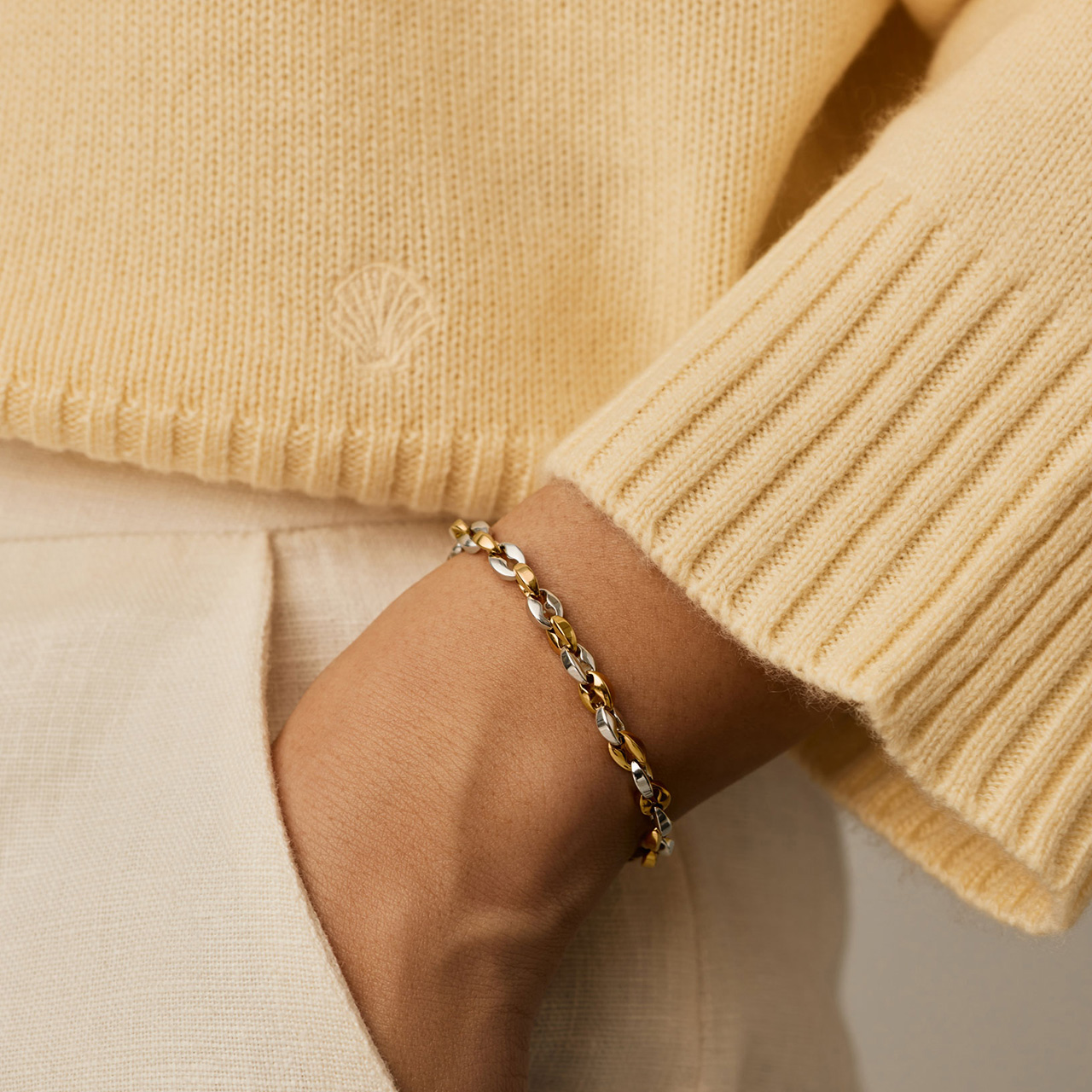 Woman wearing cream ribbed knit jumper and beige trousers with silver chain bracelet on wrist