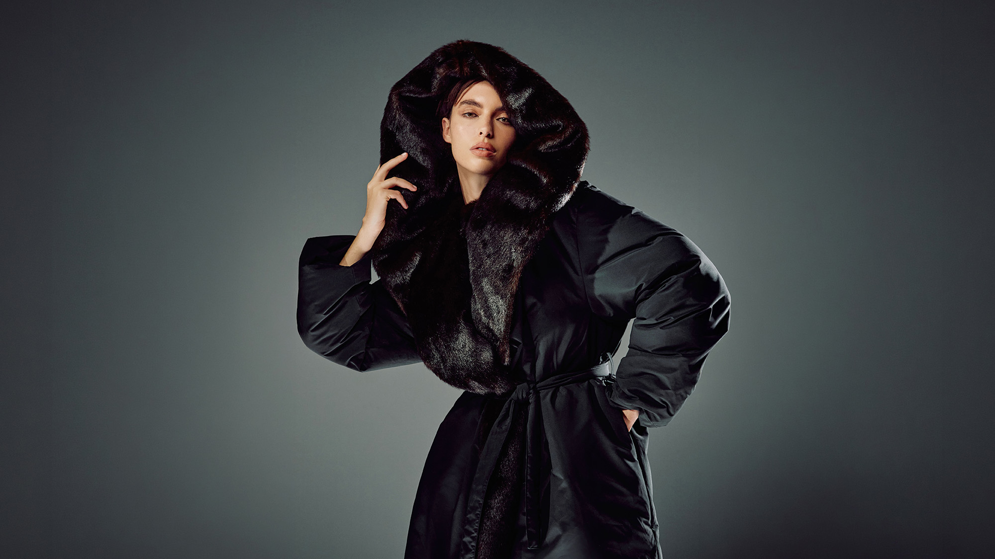 Woman wearing black puffer jacket with large fur collar hood, hand touching collar