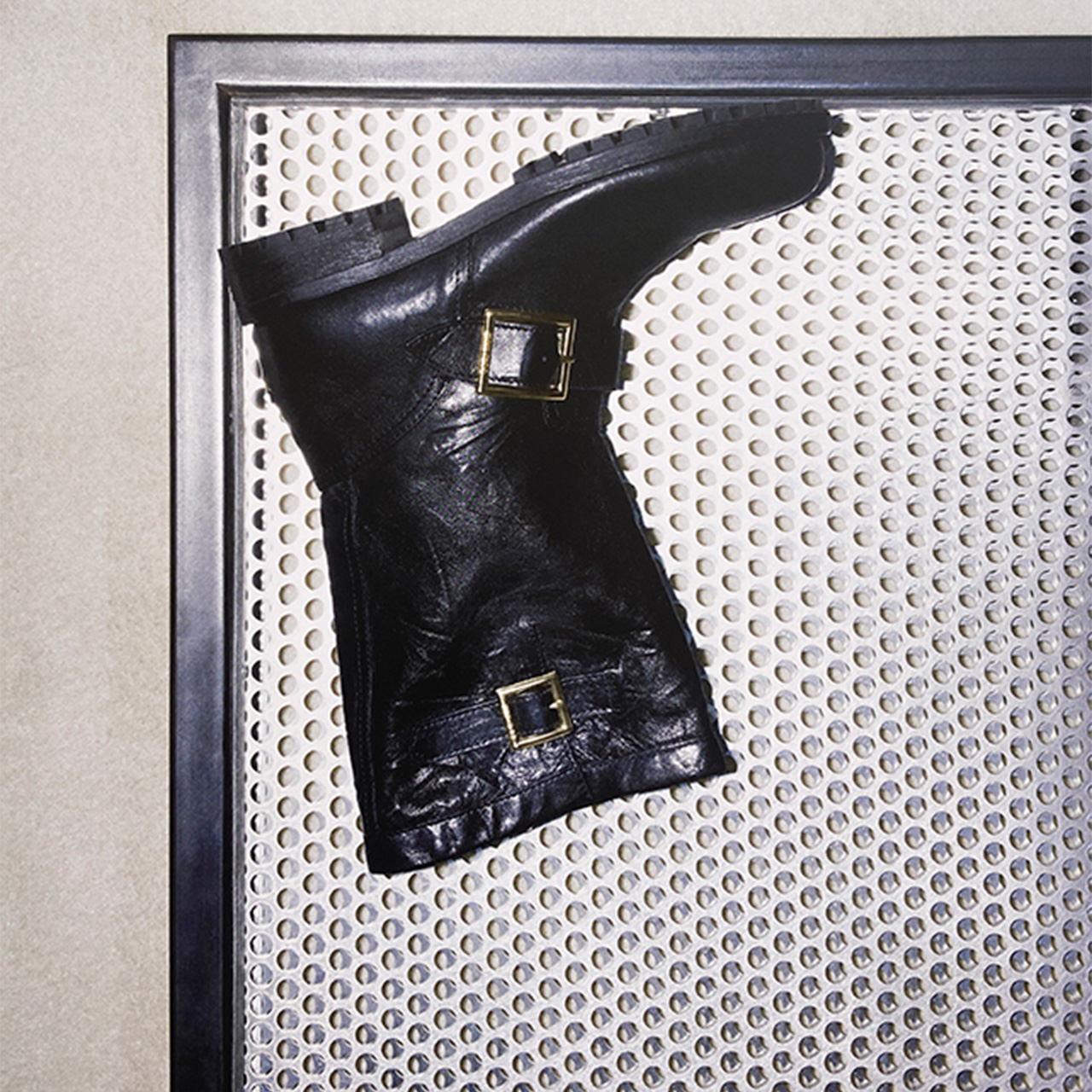 Black leather buckled boots with gold hardware displayed on perforated metal background