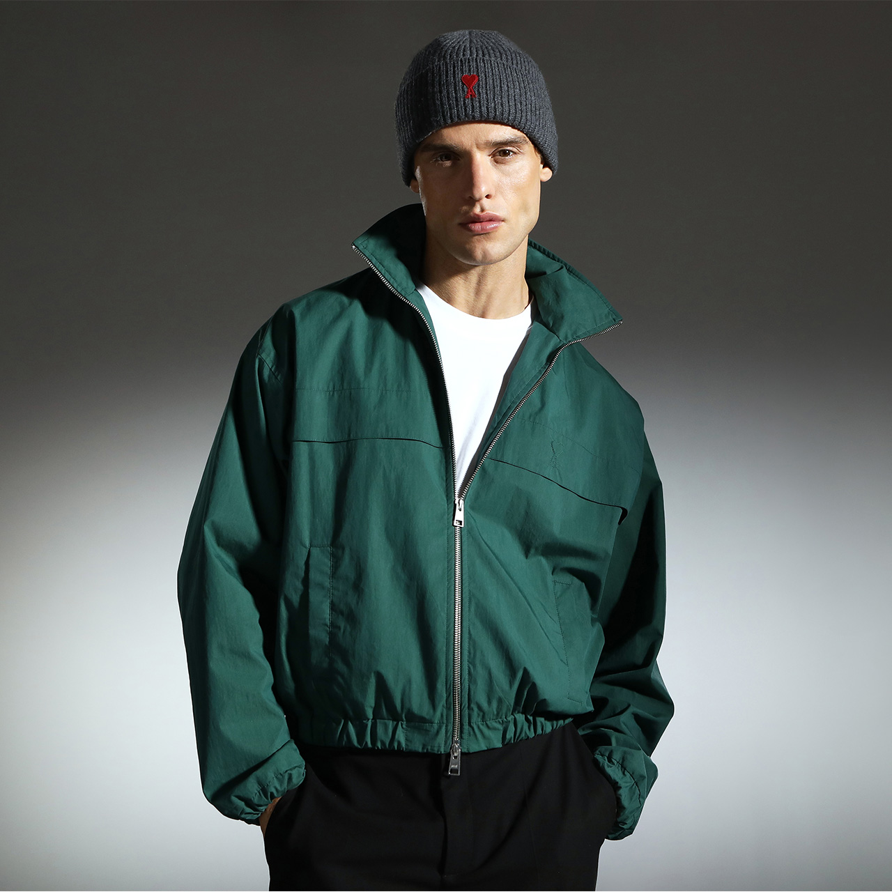 Man wearing teal zip-up jacket with grey beanie and white base layer against neutral background