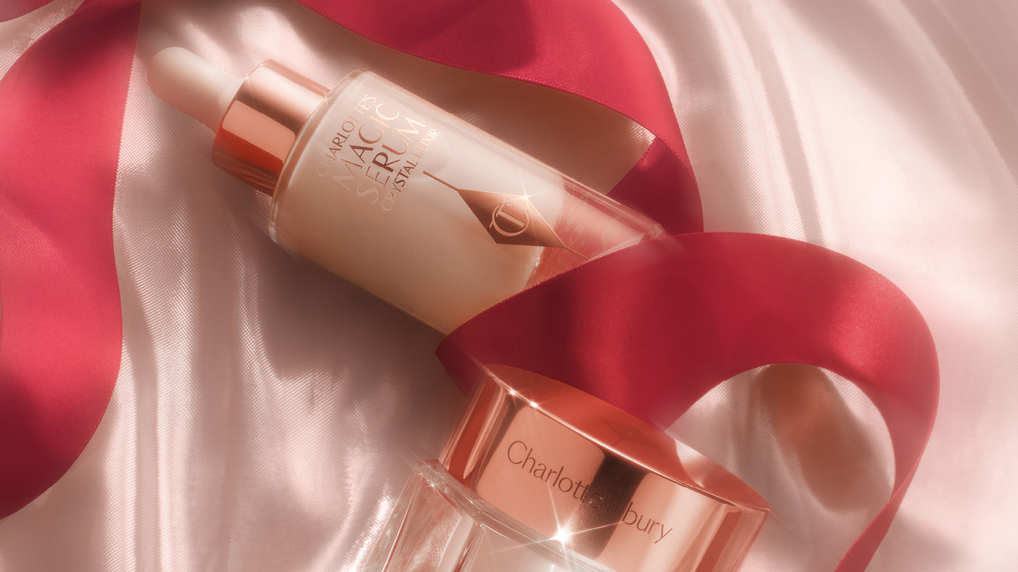 Charlotte Tilbury skincare products including mist spray and serum bottle displayed on cream and pink silk ribbons