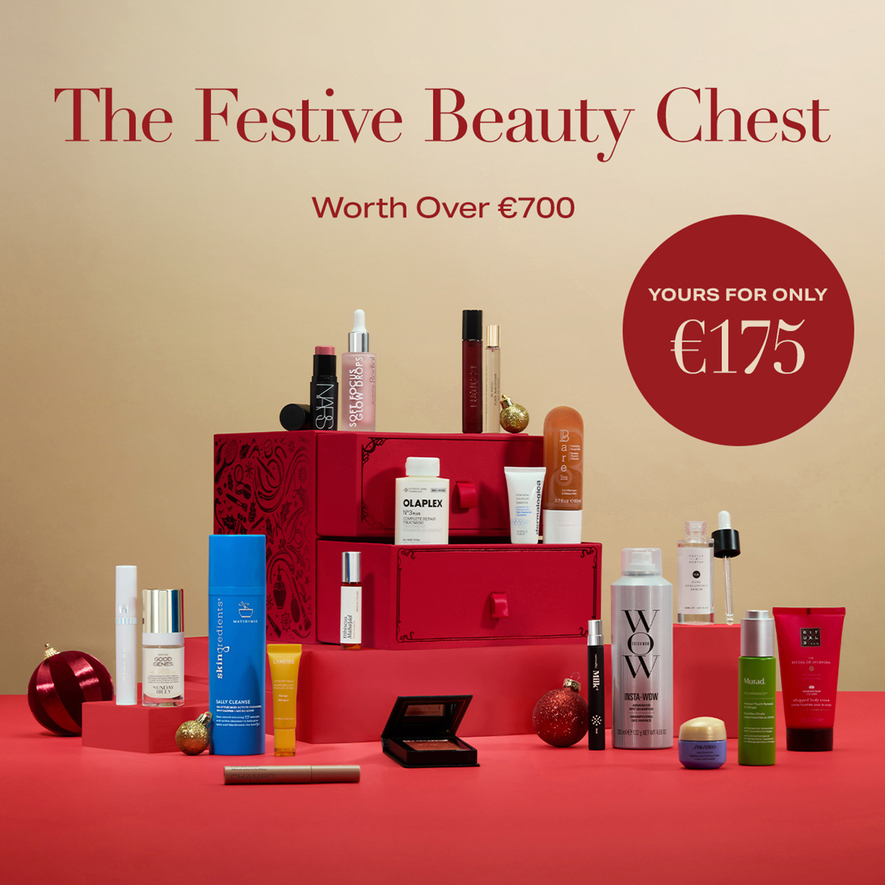 Red gift box filled with luxury beauty products including makeup, skincare, and fragrances, displayed on red surface with festive gold baubles
