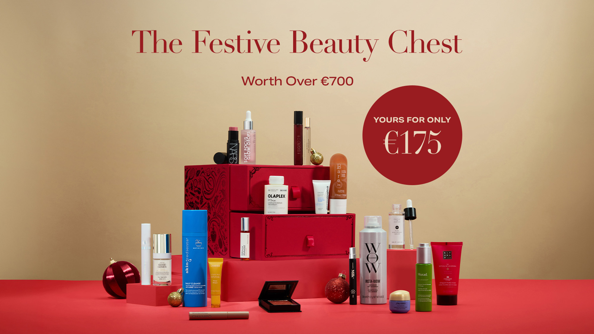 Red gift box filled with luxury beauty products including makeup, skincare, and fragrances, displayed on red surface with festive gold baubles