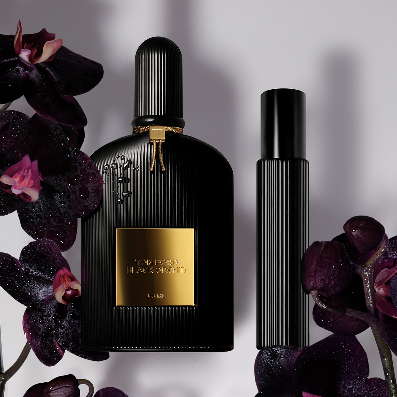 Black fragrance bottles with gold accents surrounded by dark purple orchids with pink centres