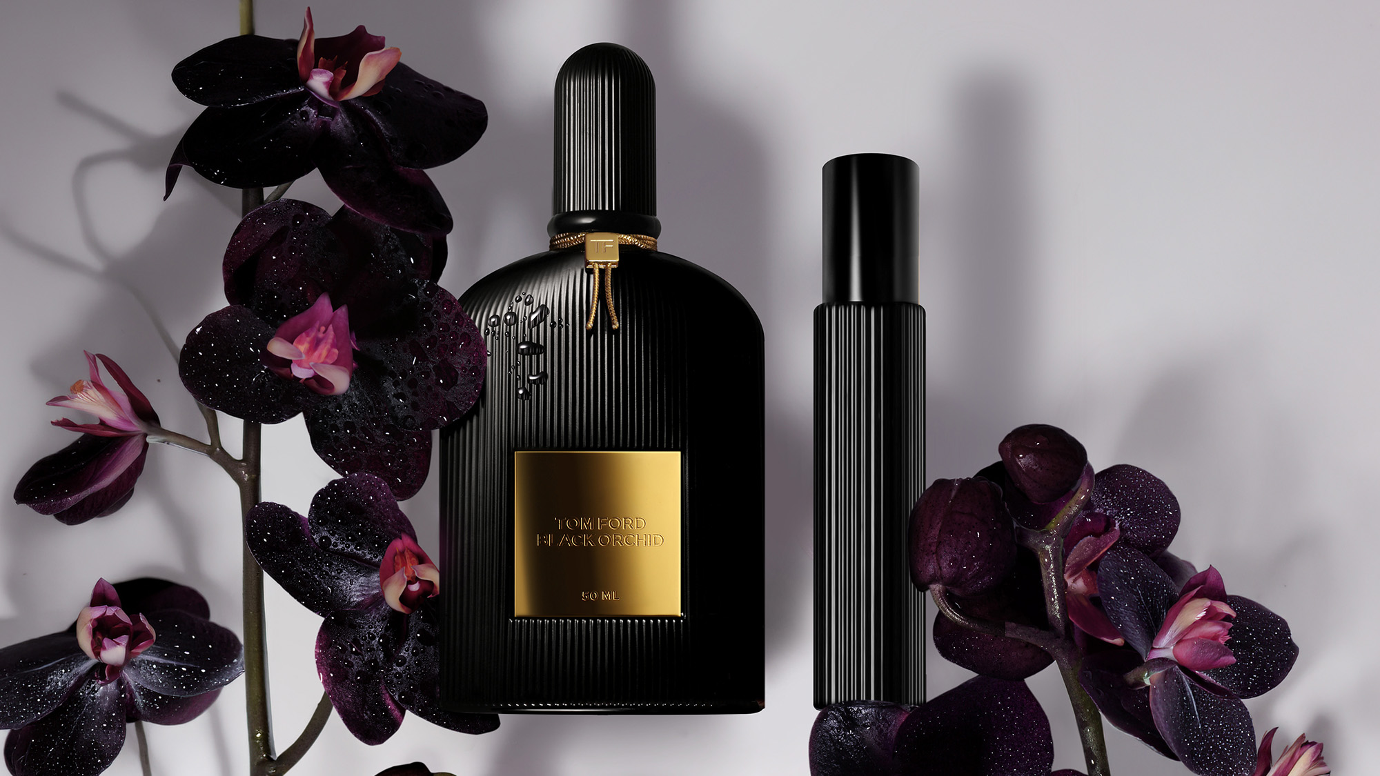 Tom Ford Black Orchid fragrance bottle with gold label surrounded by dark purple orchid flowers with pink centres