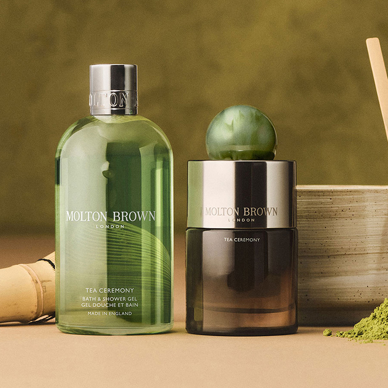 Molton Brown Tea Ceremony bath and shower gel, candle, wooden bowl and matcha whisk displayed on neutral surface