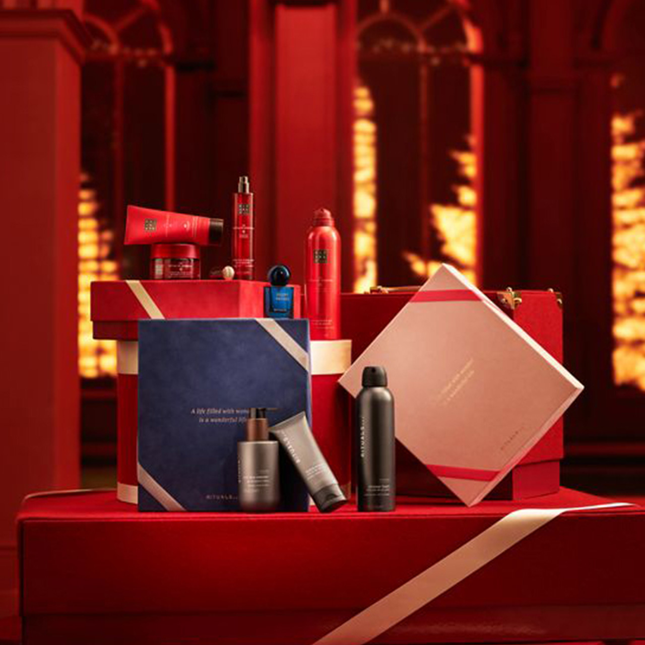 Red and navy gift sets with skincare products displayed on red tiered platforms against warm lighting