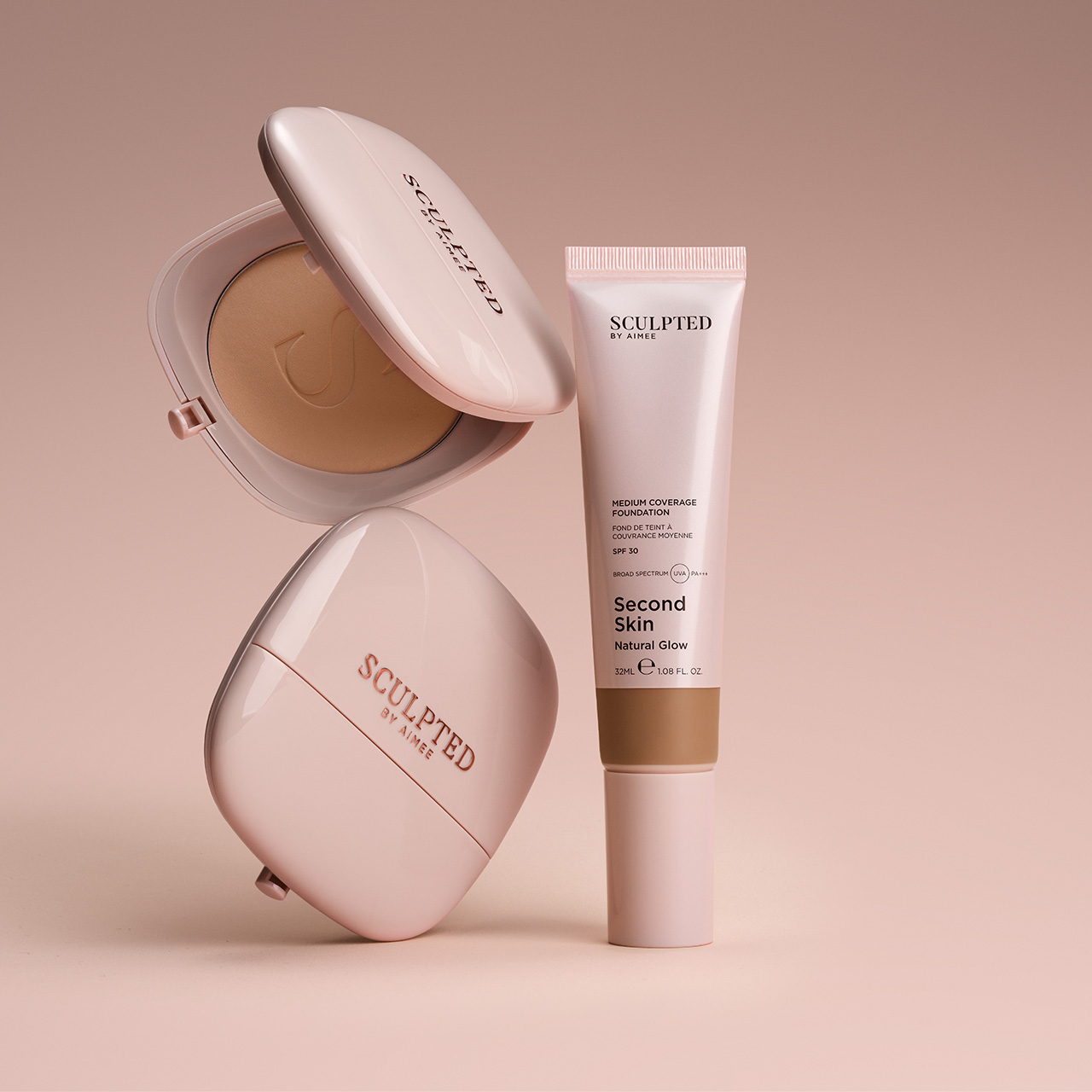 Sculpted by Aimee Second Skin foundation displayed with medium coverage foundation tube and compact powder in warm beige tone on neutral background