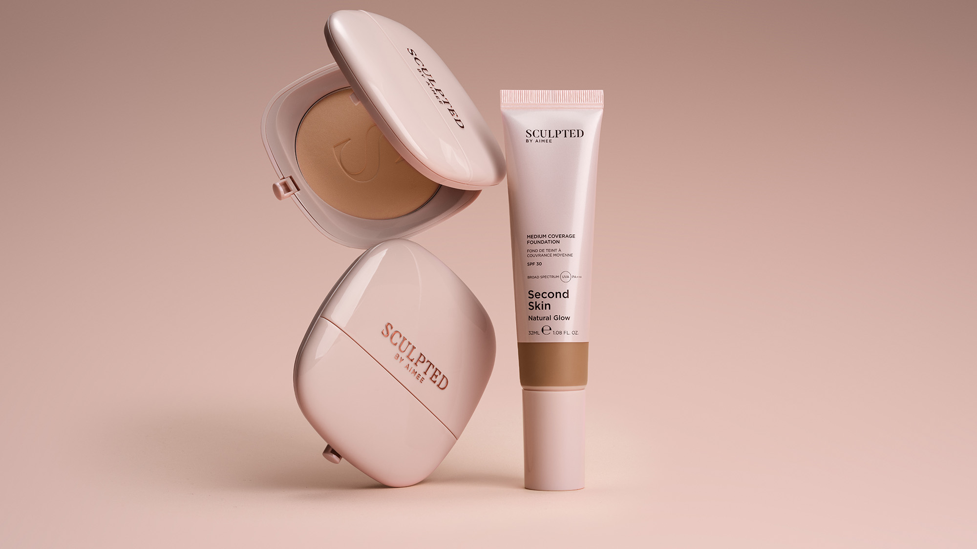 Sculpted by Aimee Second Skin foundation displayed with medium coverage foundation tube and compact powder in warm beige tone on neutral background