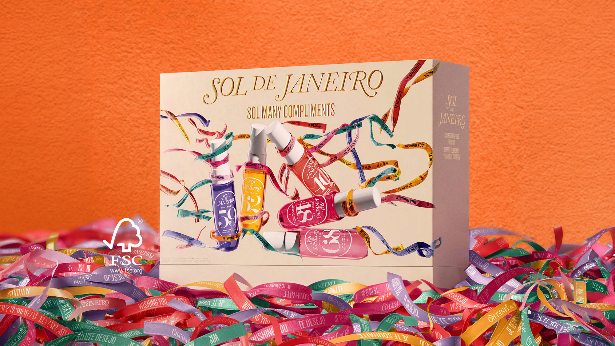 Sol de Janeiro gift set box with multiple fragrance bottles in colourful packaging surrounded by multicoloured ribbons on orange background