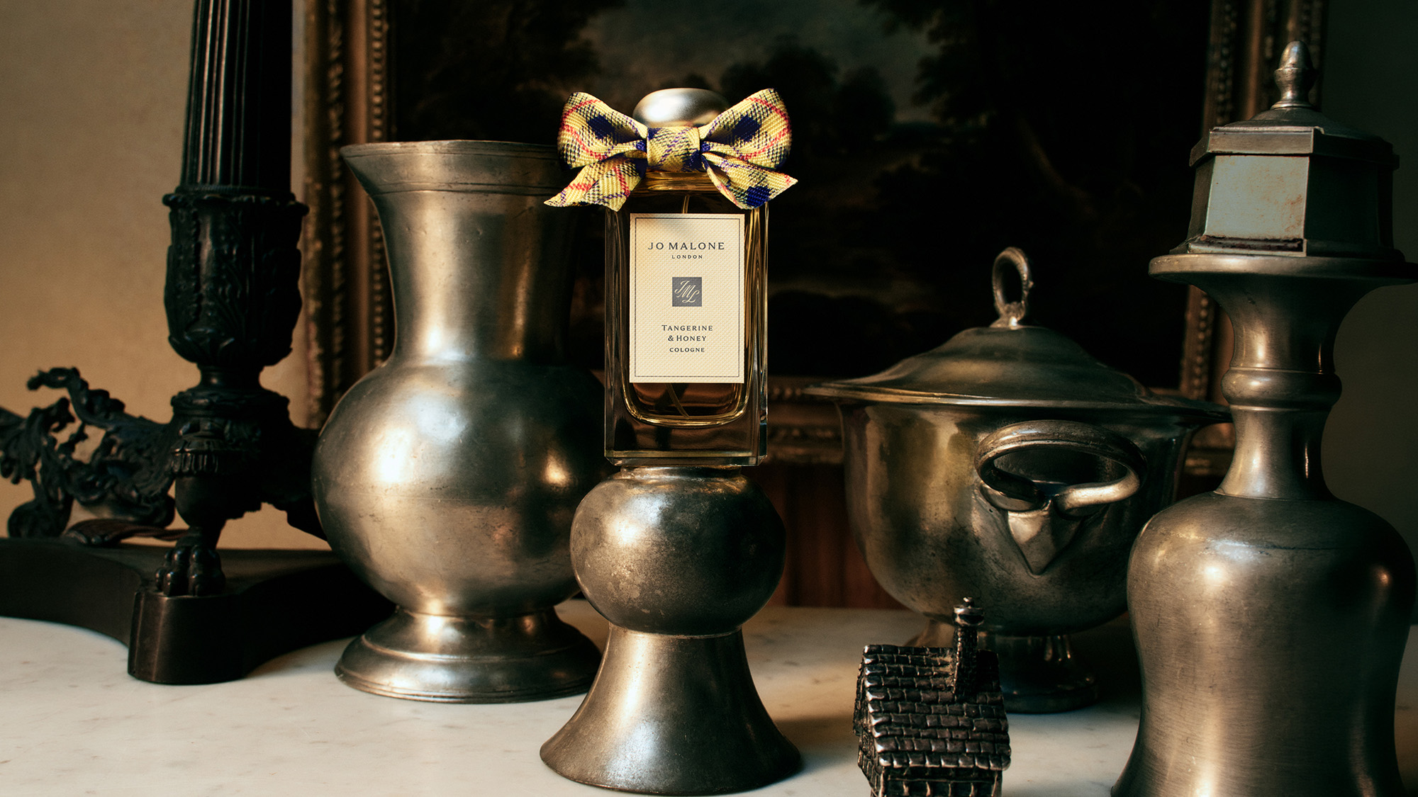 Jo Malone fragrance bottle with gold bow surrounded by vintage brass decorative objects and candlesticks