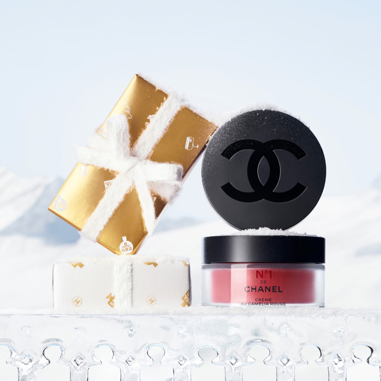Chanel cream jar with a gold wrapped gift, set against a snowy background.