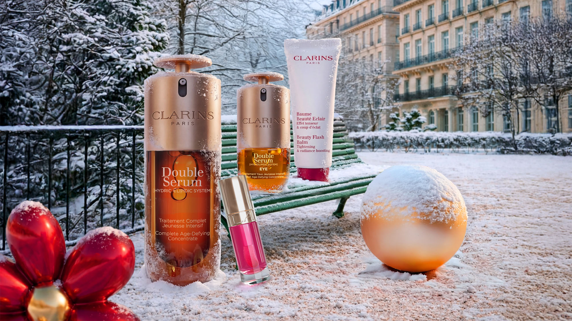 Clarins Double Serum, Eye Serum, Beauty Flash Balm and lipstick arranged in a snowy Parisian garden with red baubles and gold ornaments.