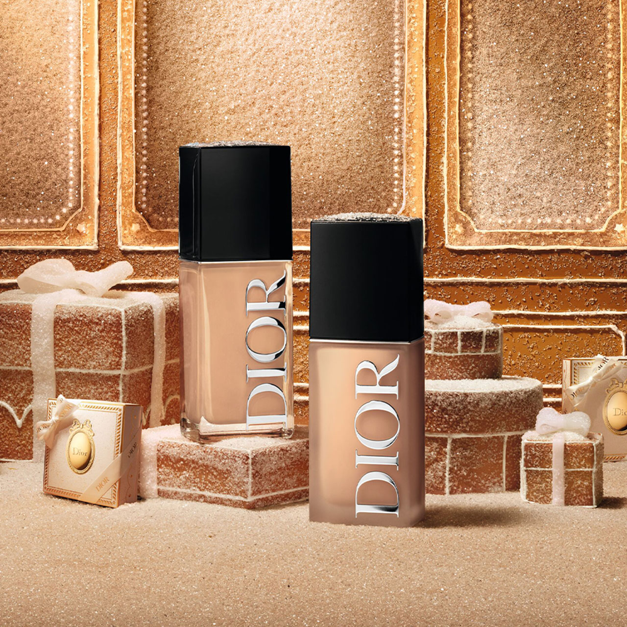 Dior liquid foundation and lip product bottles arranged on gold brick-textured set with wrapped gifts