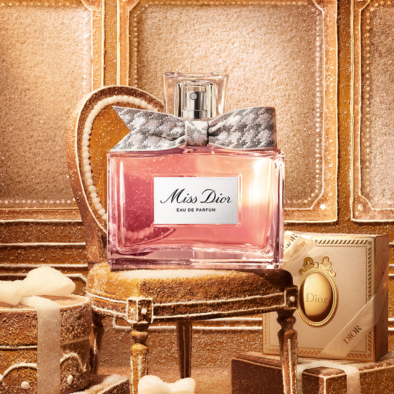 Miss Dior eau de parfum bottle with grey bow, displayed with beige luxury gift box and accessories on golden background