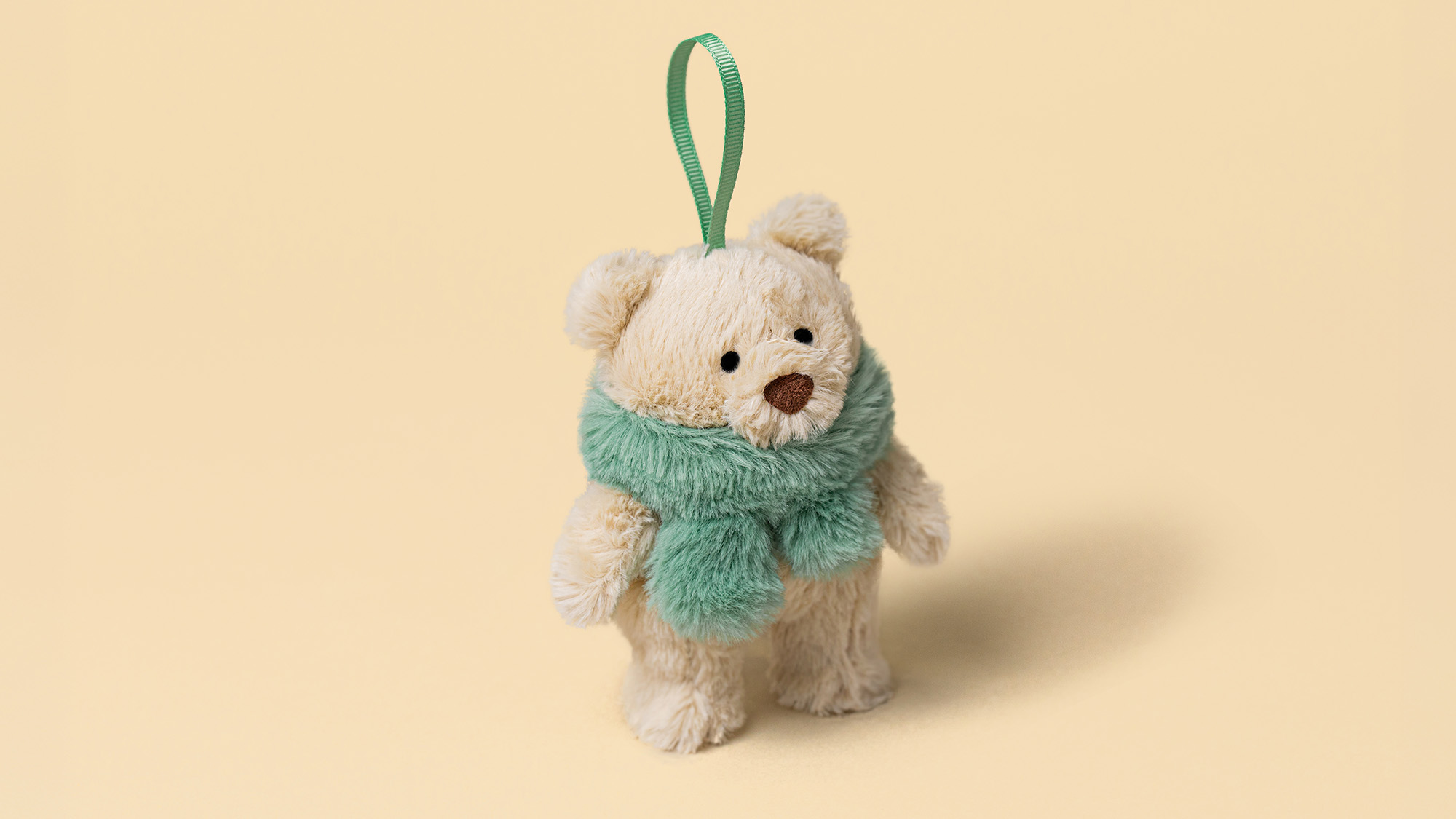 Cream teddy bear wearing a sage green scarf with matching ribbon loop against a beige background
