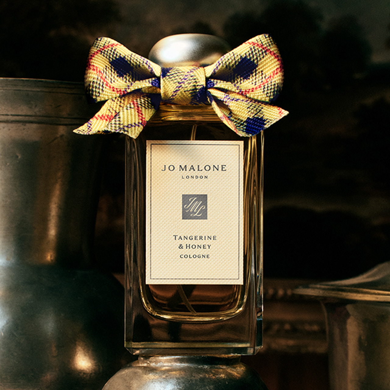 Tangerine & Honey cologne bottle with gold cap and colourful tartan ribbon bow on dark background.