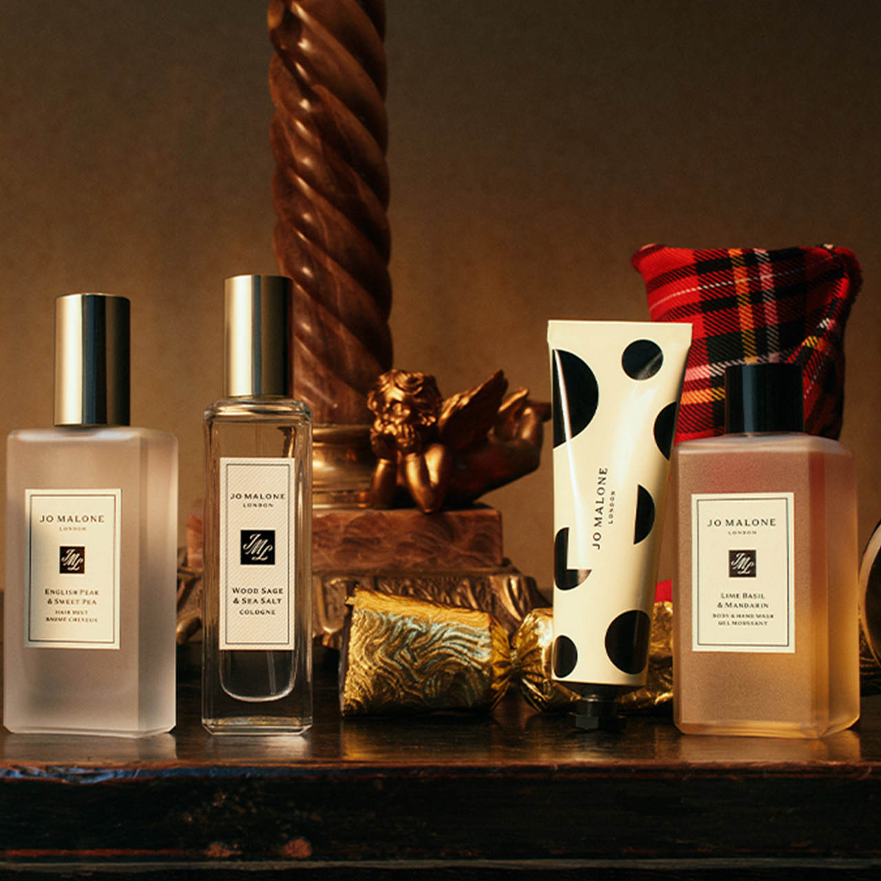 Arrangement of travel-sized fragrance and body care products including English Pear, Wood Sage, and Lime Basil with red tartan fabric.