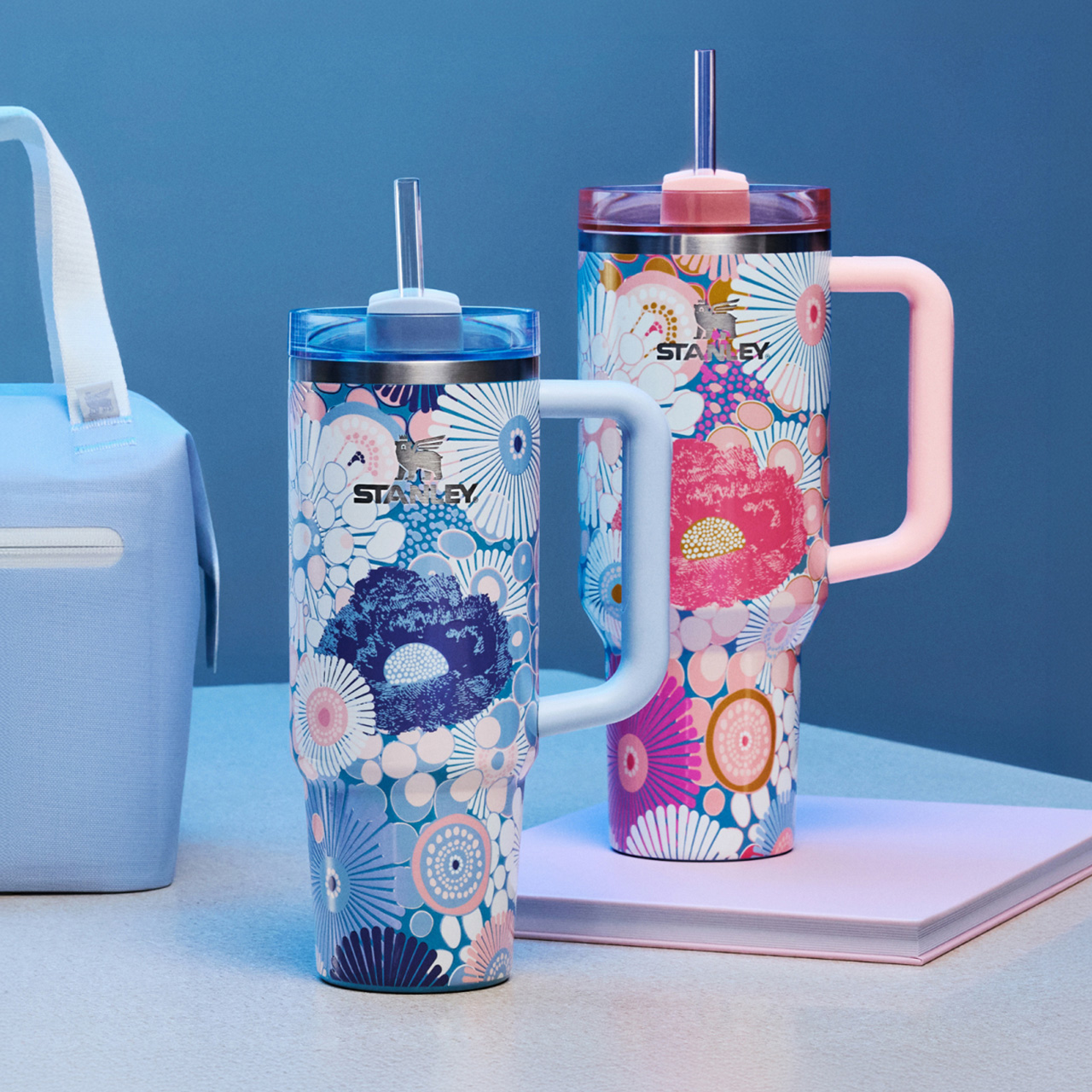 Stanley drinkware collection featuring a light blue insulated bag, patterned tumbler with straw, and large water bottle with pink handle