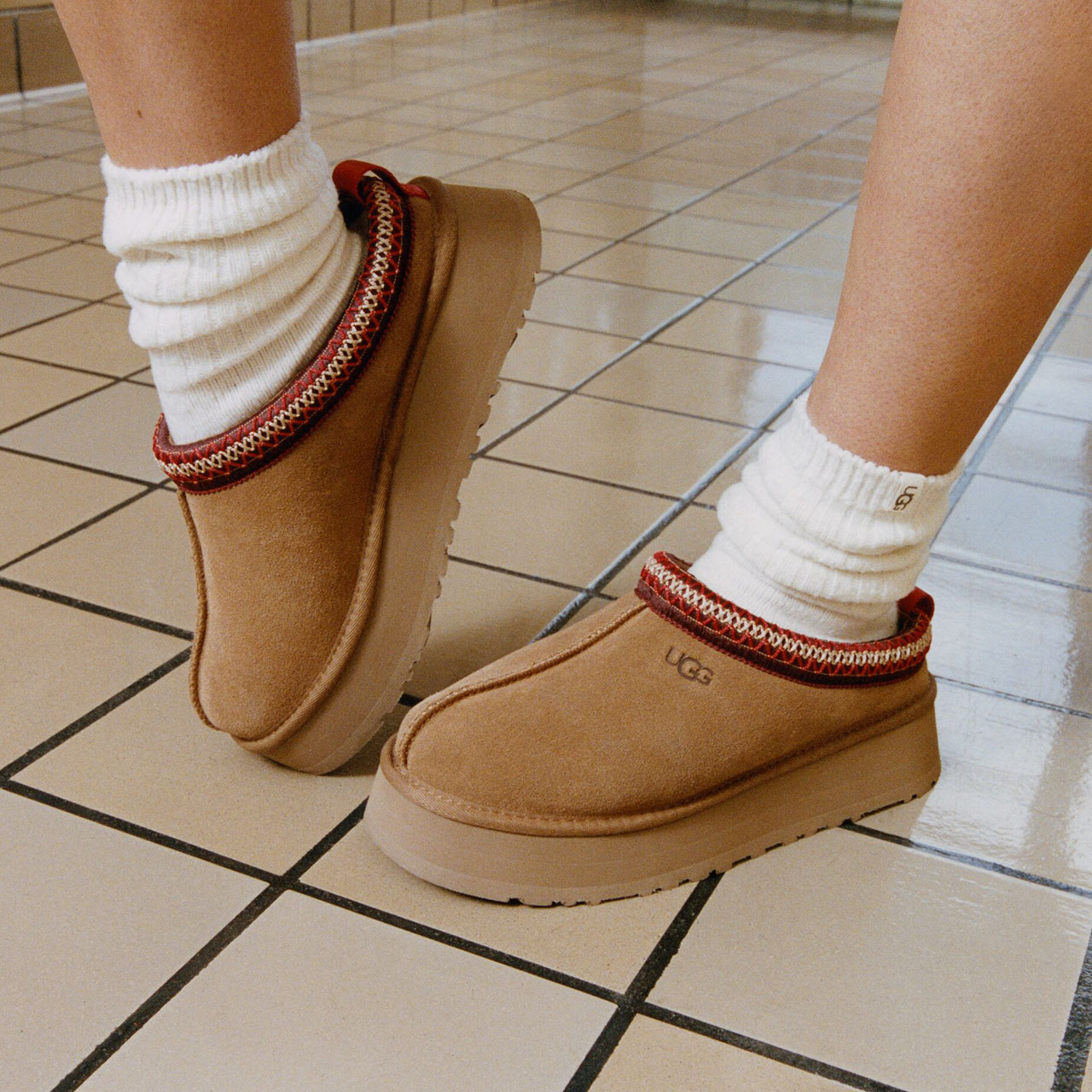 Person wearing cream socks and tan suede boots with red trim detail standing on tiled floor