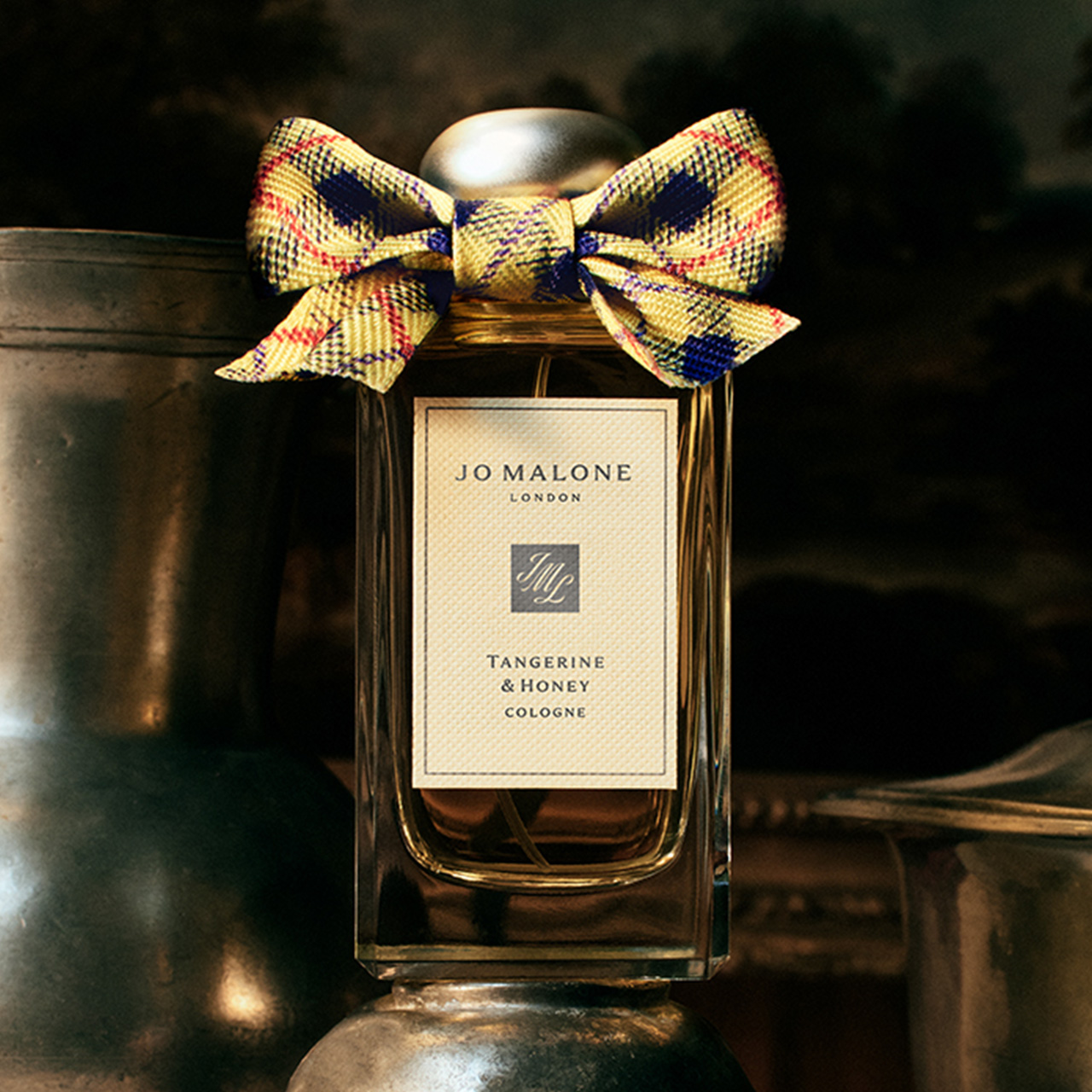 Jo Malone London Tangerine & Honey cologne bottle with decorative yellow and navy ribbon bow, displayed with silver vessels