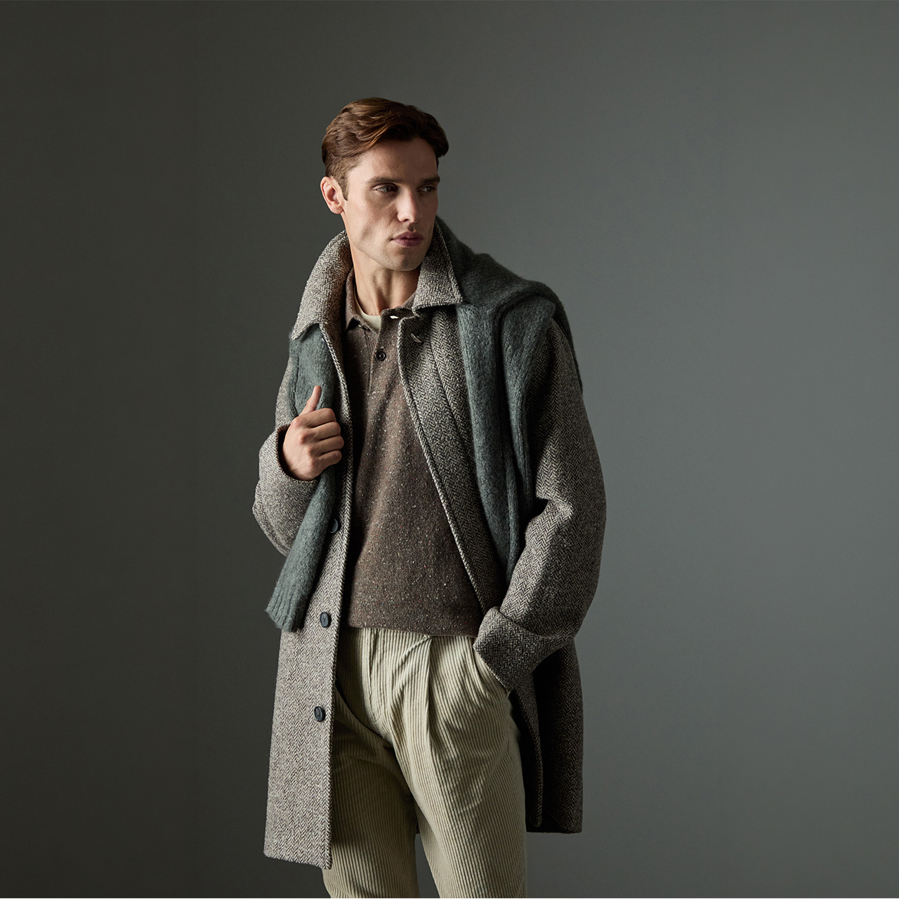 Man wearing grey wool coat over textured charcoal jumper and cream ribbed trousers against neutral background